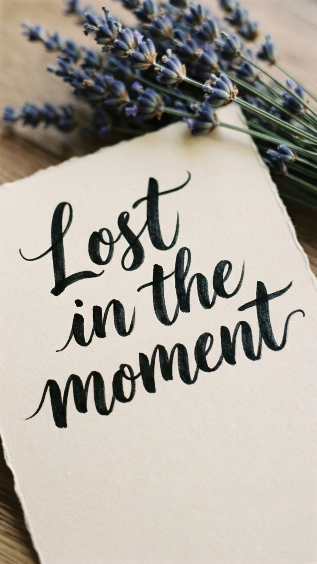 米色紙上以黑色草書寫著「Lost in the moment」，旁邊有乾薰衣草在木頭上。