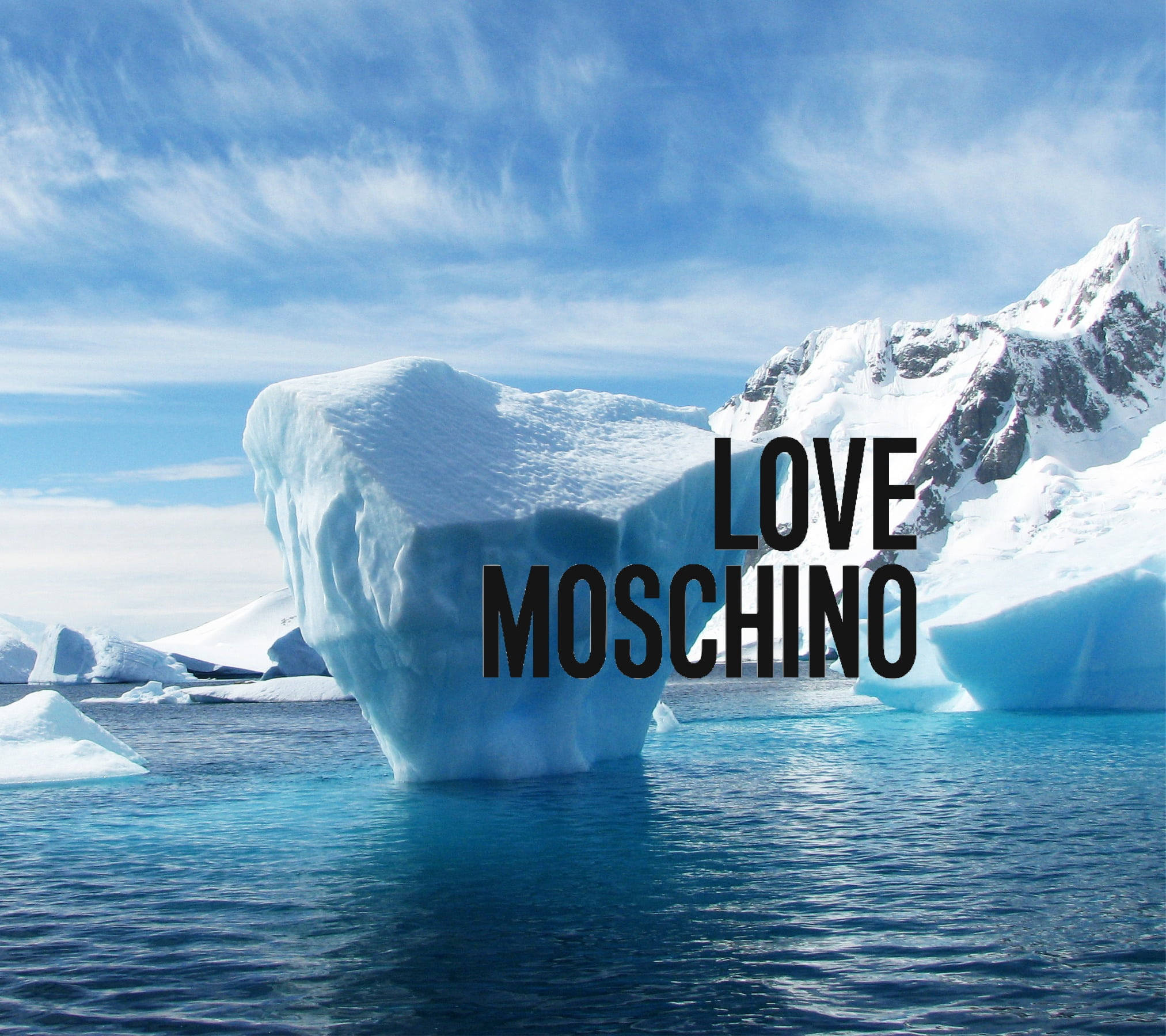 Love Moschino 冰山 壁紙 — 一座巨大的冰山漂浮在清澈的藍色海水中，白雪覆蓋的山脈在明亮的藍天下。