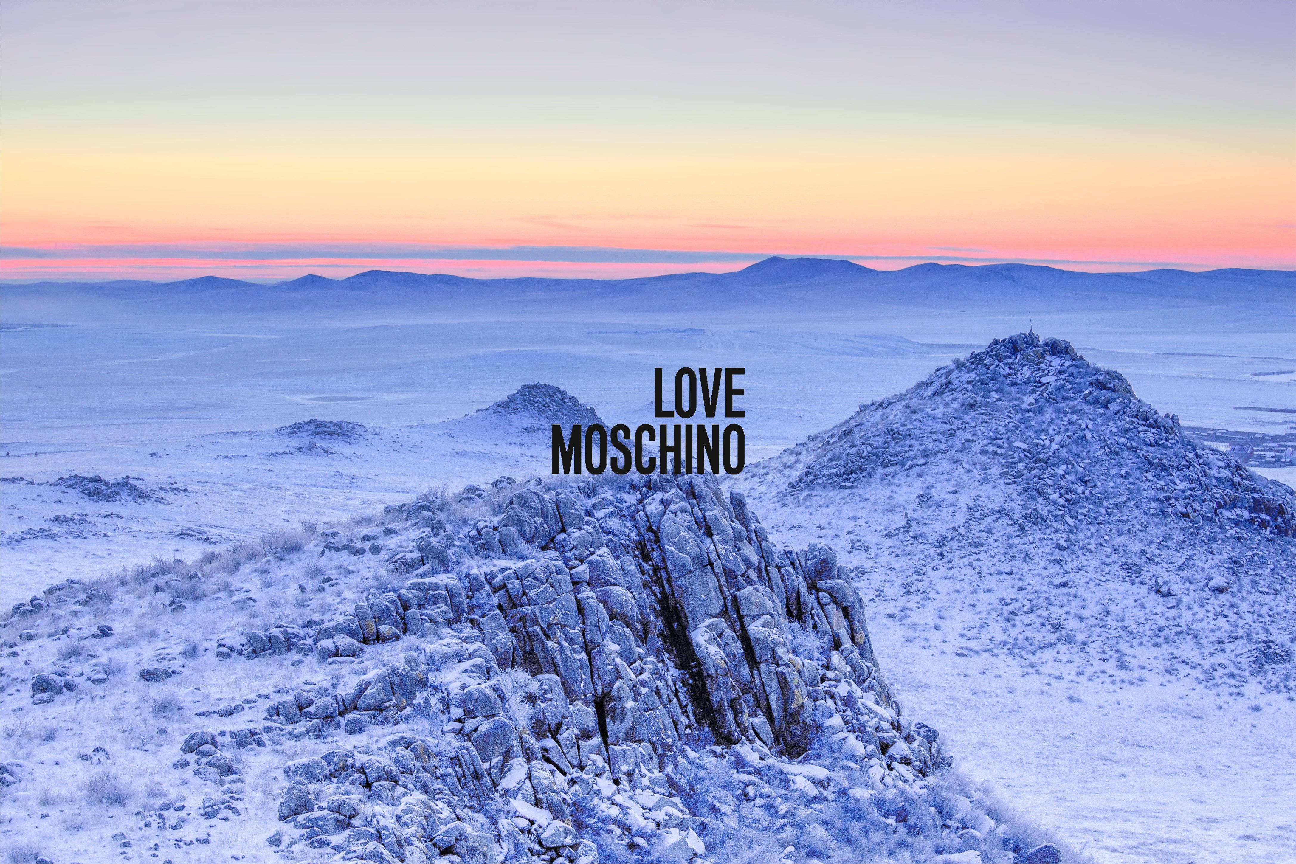 Love Moschino 雪山 壁紙 — 白雪覆蓋崎嶇的岩石和遠山，在柔和的粉紅色和橙色日出天空下。