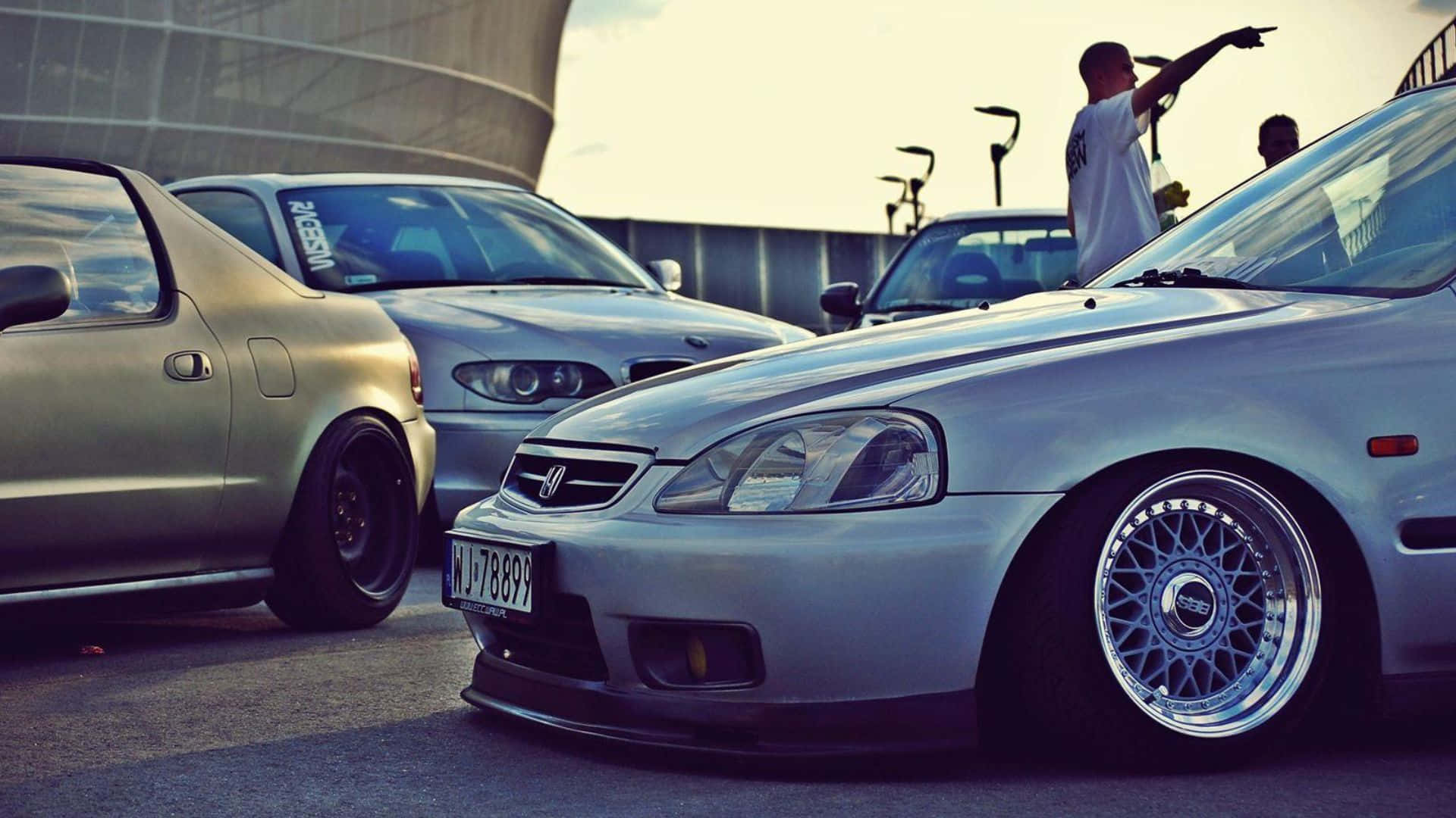Honda Civic Del Sol 桌布 壁紙 — 低調改裝車配備自訂輪圈，停放在陽光明媚的城市空地，一人正朝它們做手勢。