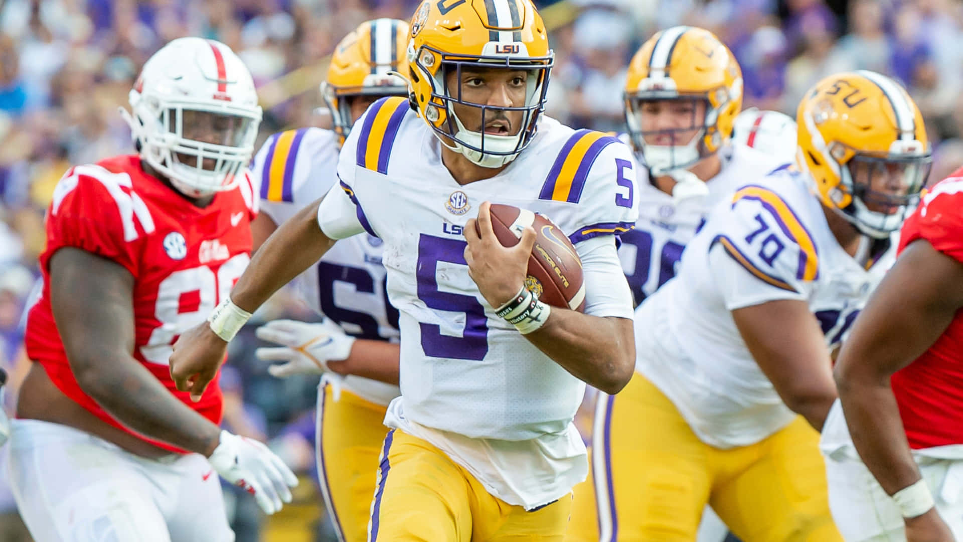  壁紙 — LSU 四分衛 5 號在緊張的大學美式足球比賽中，在對手逼近的情況下帶球奔跑。