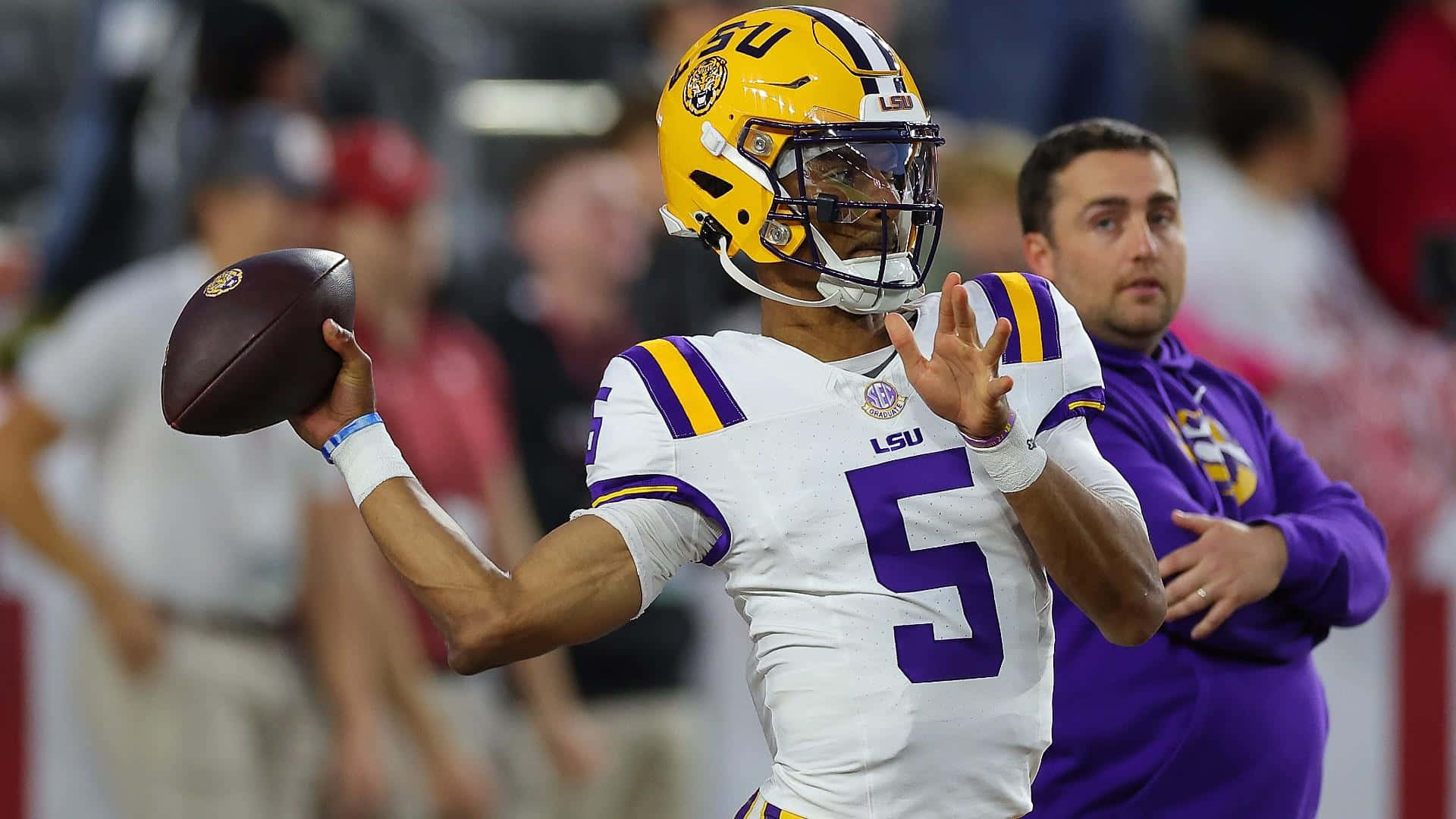  壁紙 — LSU 足球四分衛身穿白色和紫色制服，在夜間比賽中於體育場燈光下投擲足球。