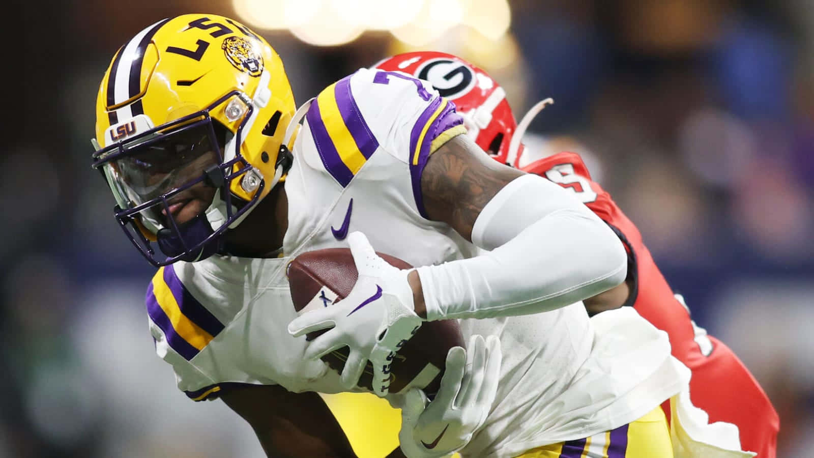  壁紙 — LSU 足球員戴住黃色頭盔，喺被紅色佐治亞州防守球員攔截時緊抱住個波。