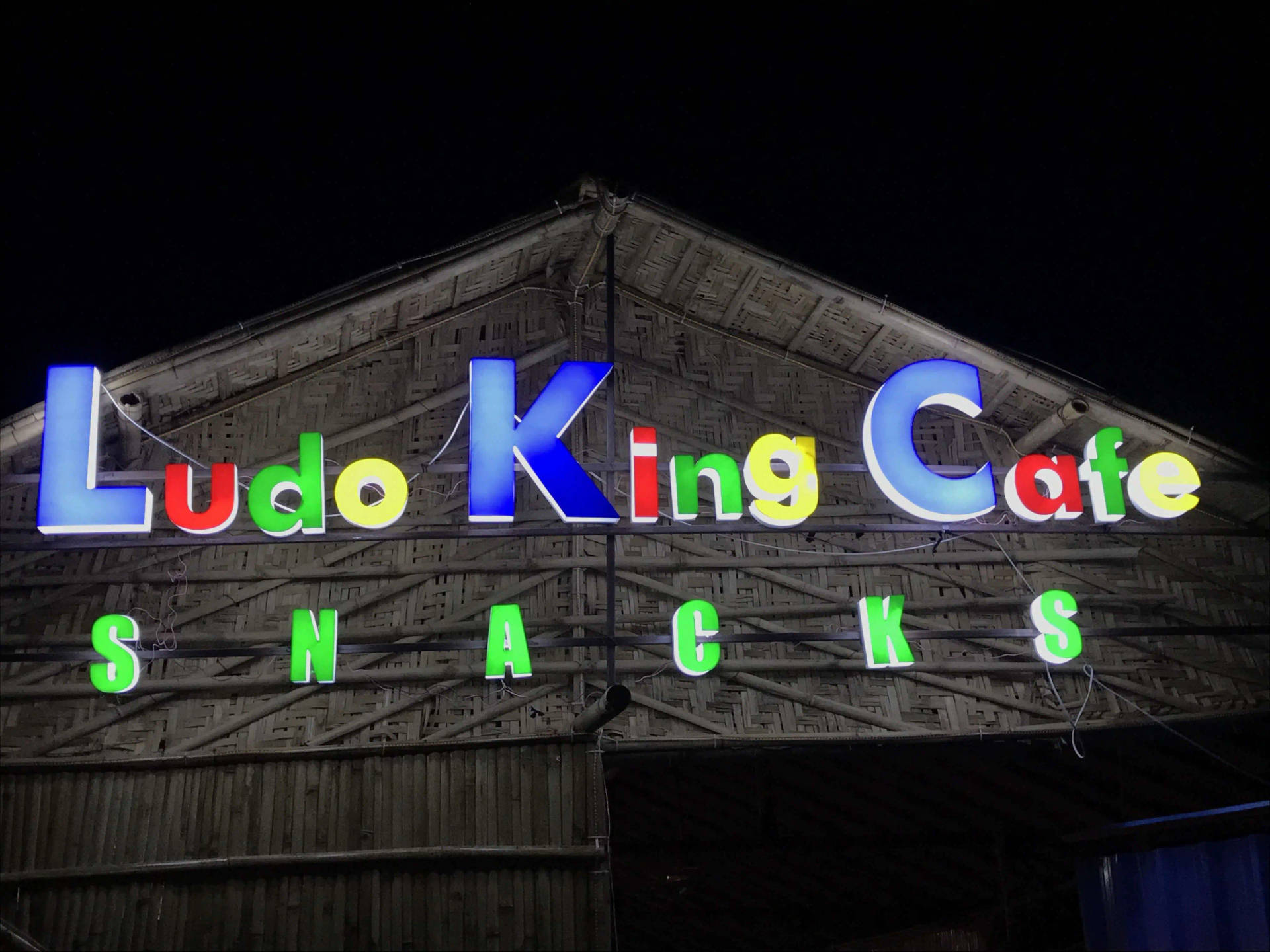 竹建築上 Ludo King Cafe Snacks 的彩色霓虹招牌（夜間）。