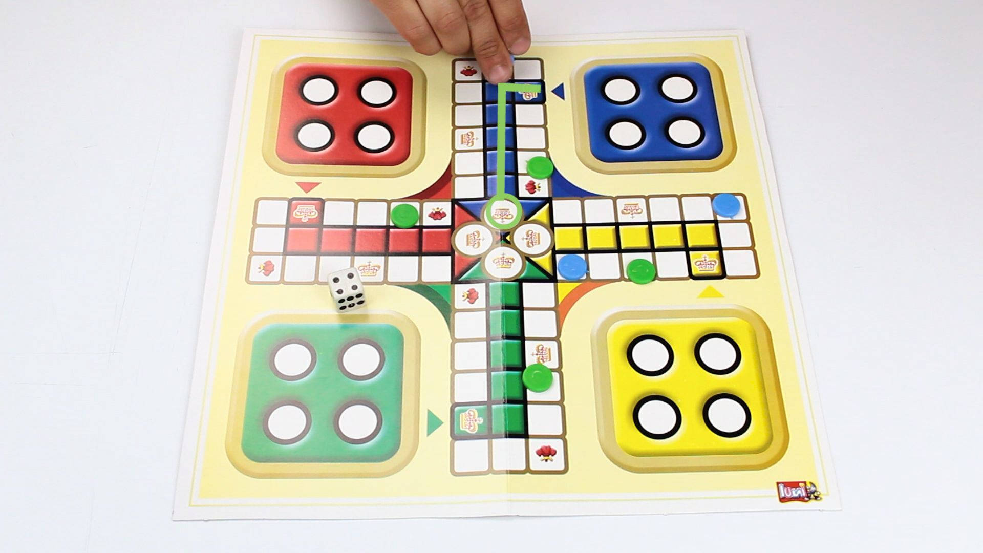 手在色彩繽紛的Ludo棋盤上玩綠色籌碼