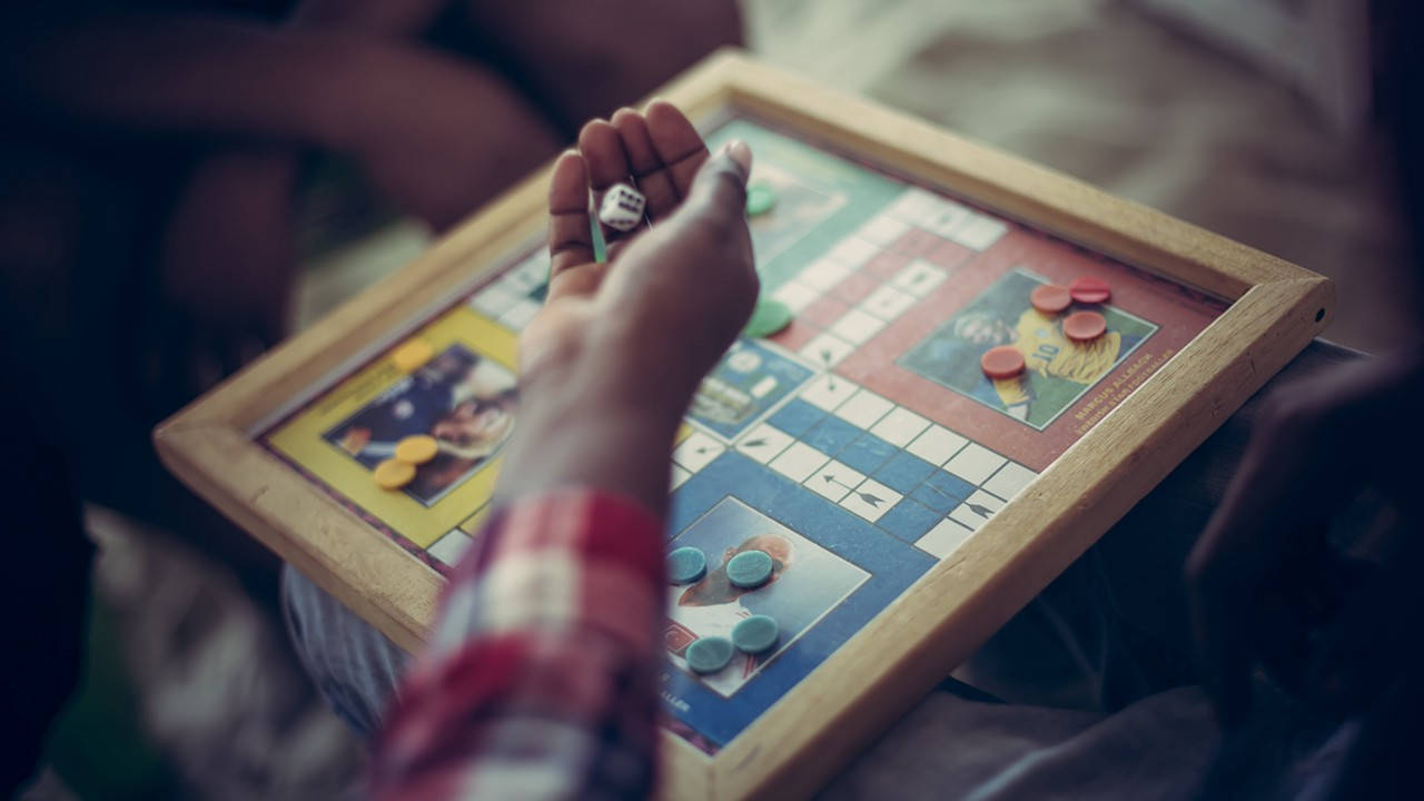 手舉骰子在色彩繽紛的棋盤遊戲上方，有籌碼和卡片。