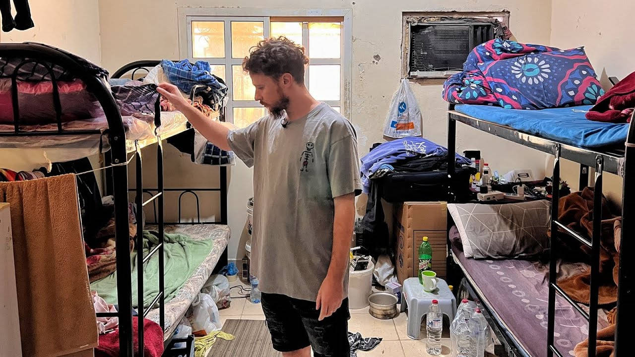 男子在雜亂的宿舍房間裡整理衣服，房間裡有雙層床。