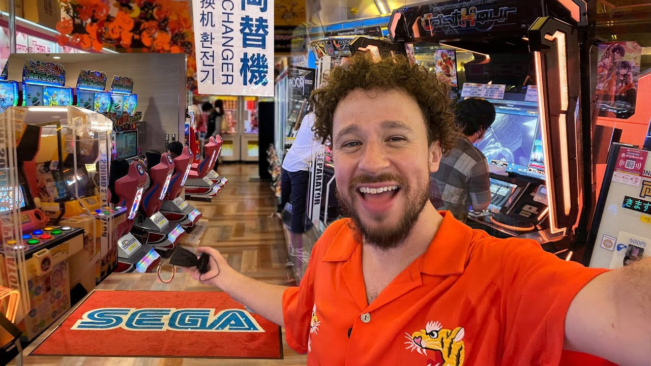 穿著橙色襯衫的男子在遊戲機中心微笑，旁邊有Sega遊戲機。