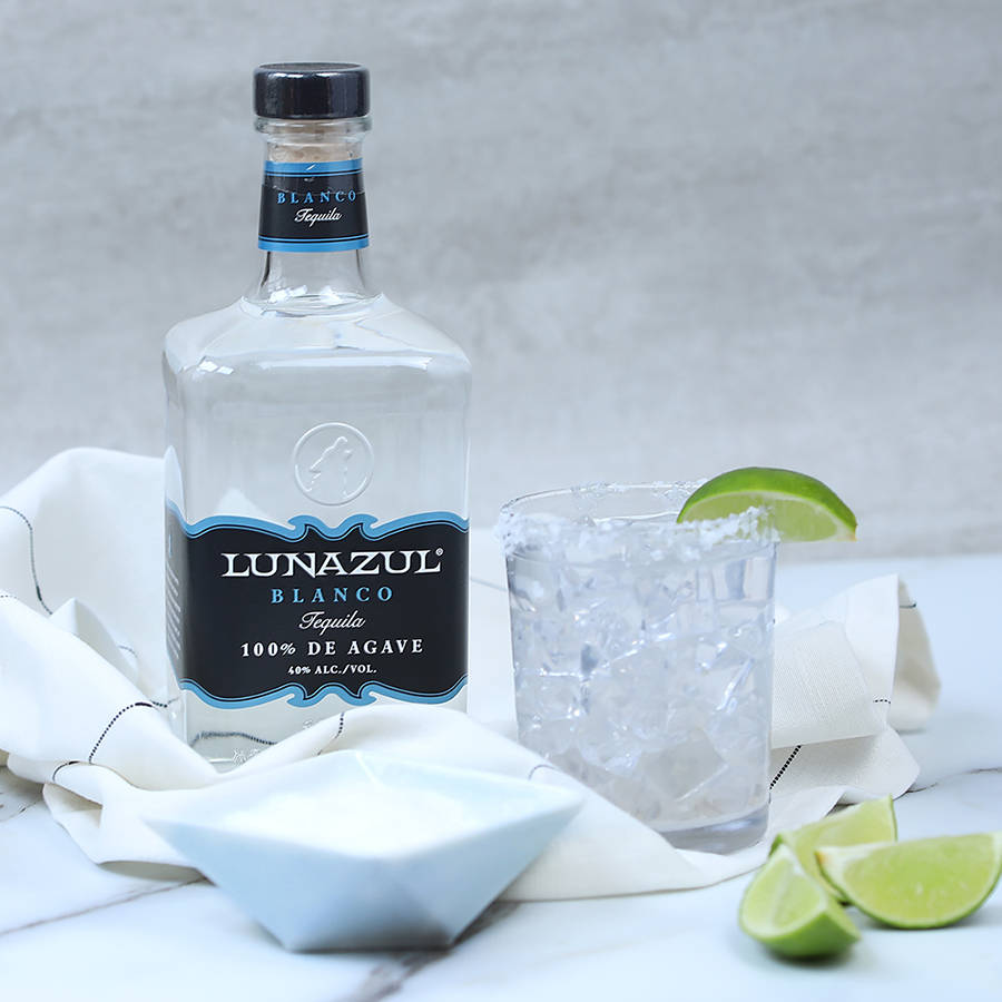 Lunazul Blanco 蒸餾龍舌蘭酒 壁紙 — 一瓶透明的Lunazul Blanco龍舌蘭酒放在白色布上，旁邊是一個鹽邊玻璃杯，裝滿冰塊和青檸。