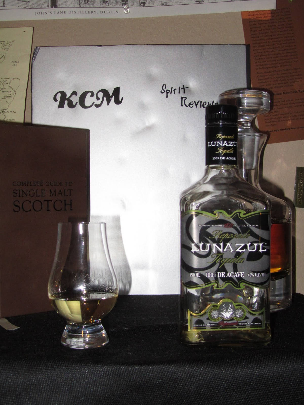 Lunazul Reposado 玻璃杯 壁紙 — 一瓶Lunazul龙舌兰酒放在一个深色桌子上，旁边有一个品酒杯和威士忌书籍。