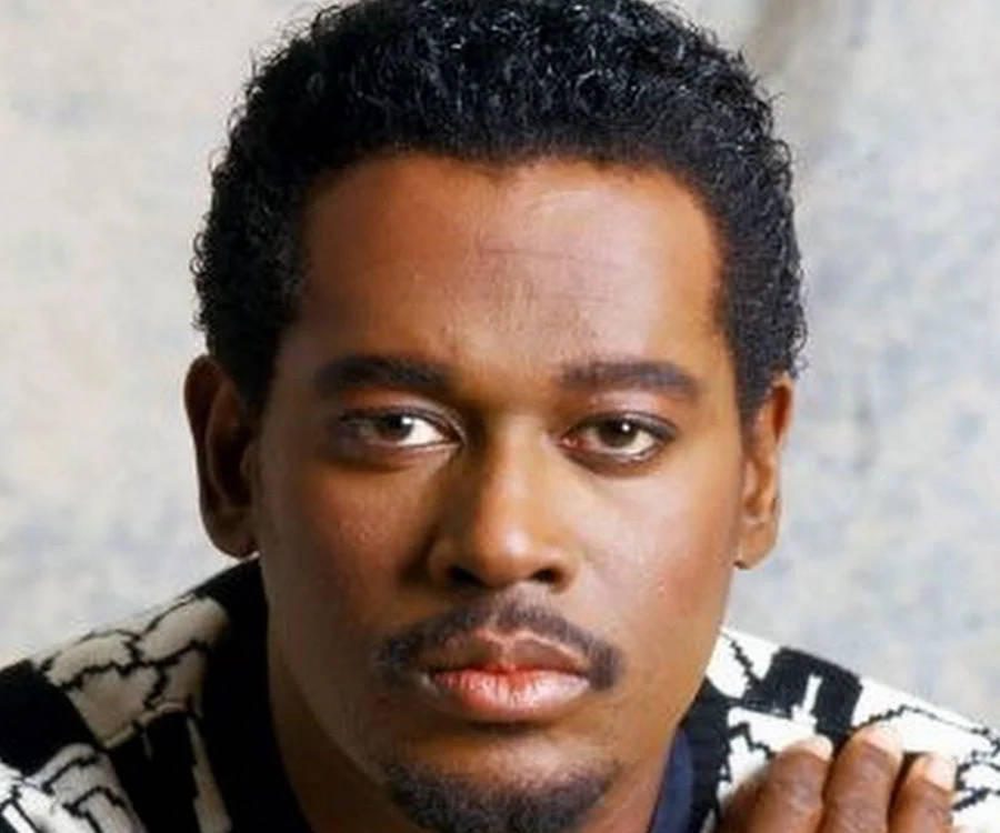 傳奇唱片製作人Luther Vandross 壁紙 — 一個近距離肖像，一個深色捲髮和鬍鬚的男人，穿著黑白圖案毛衣，背景是紋理灰色。