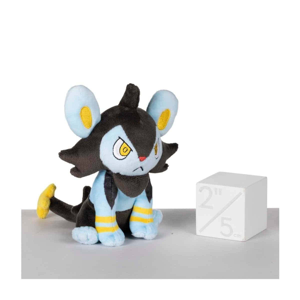 Luxio 毛絨玩具與白色方塊 壁紙 — 一隻Pokémon Luxray毛公仔坐在灰色表面上一個標有2英寸5厘米的白色立方體旁邊。
