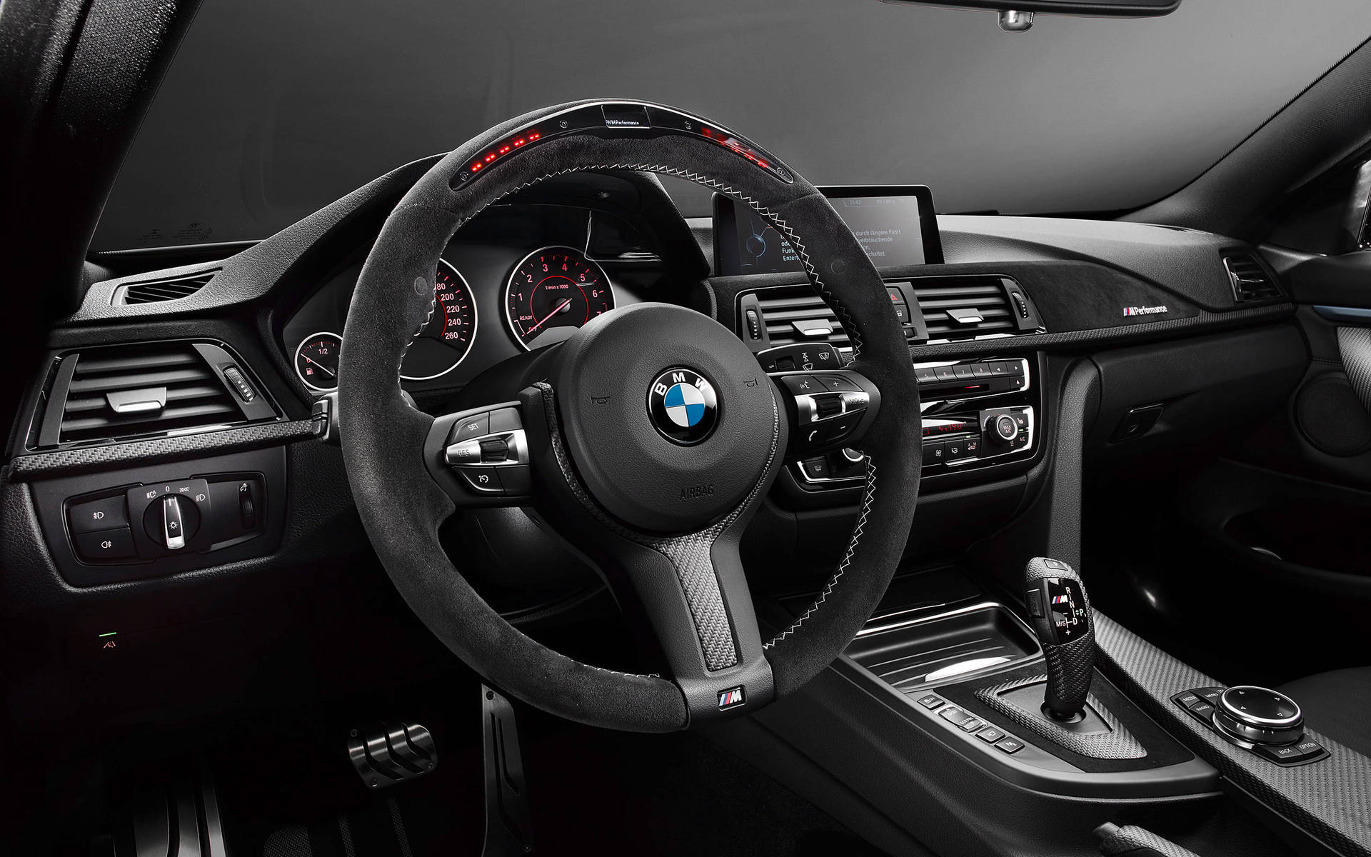 黑色BMW M汽車內飾，帶有紅色發光儀表和碳纖維飾條。