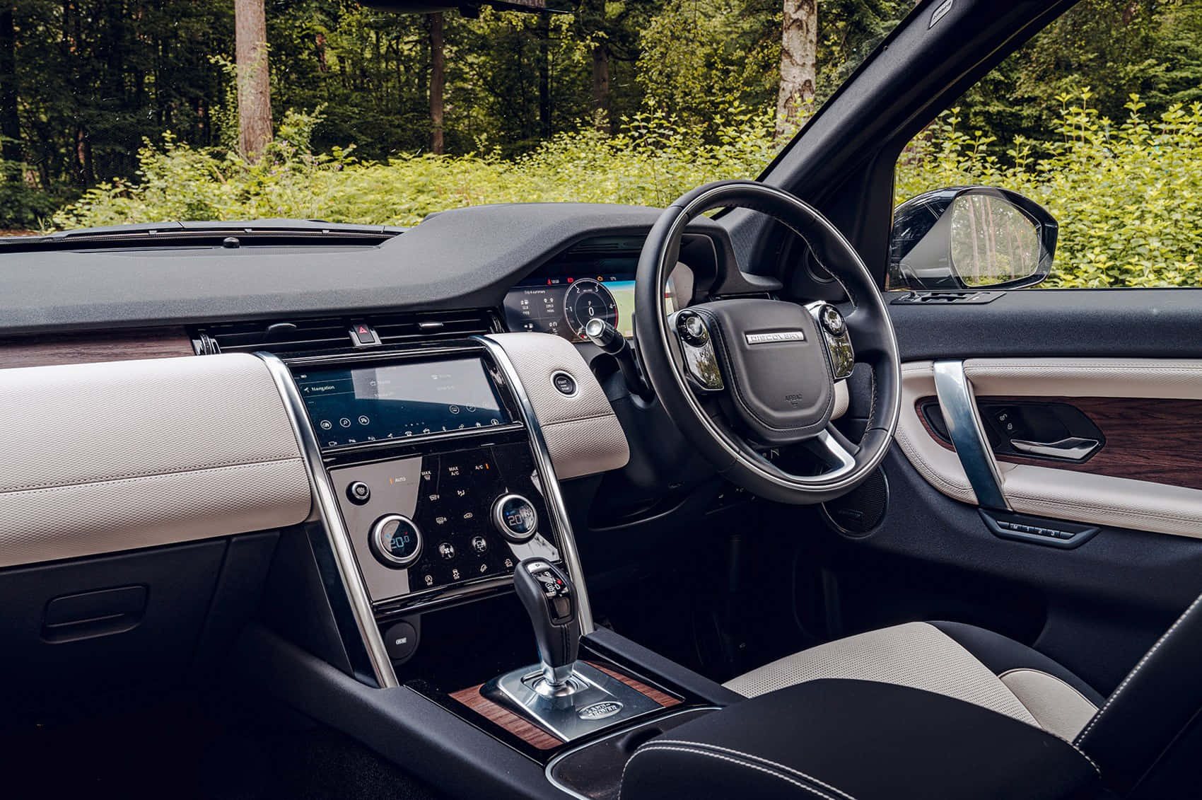 Land Rover Discovery 桌布 壁紙 — 豪華車內飾，配米色皮革和木飾，從駕駛座視角，車外有森林。