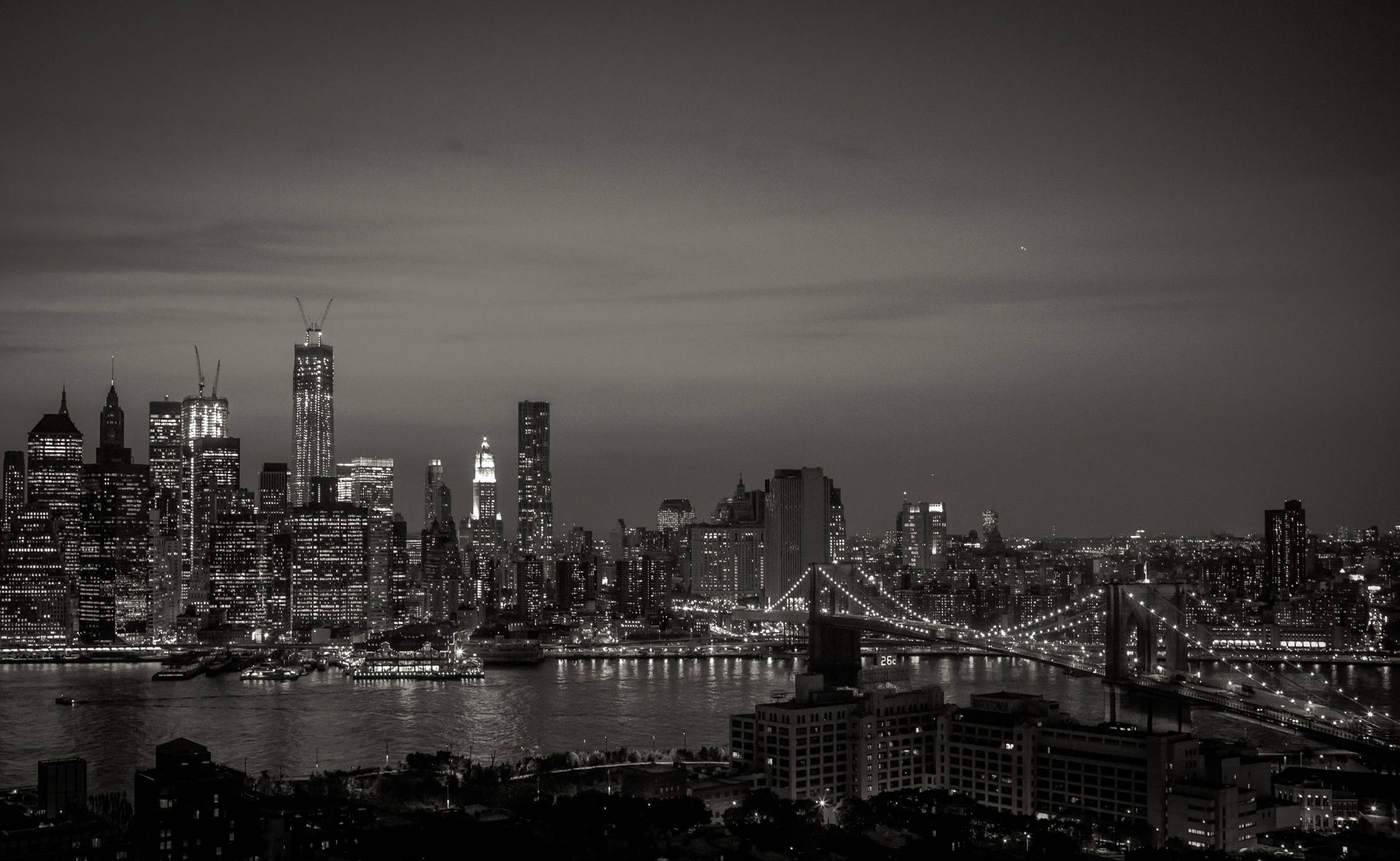 黑白 iPhone 紐約夜景燈光 壁紙 — 紐約的單色夜景，照亮的高樓大廈和布魯克林大橋橫跨河流。