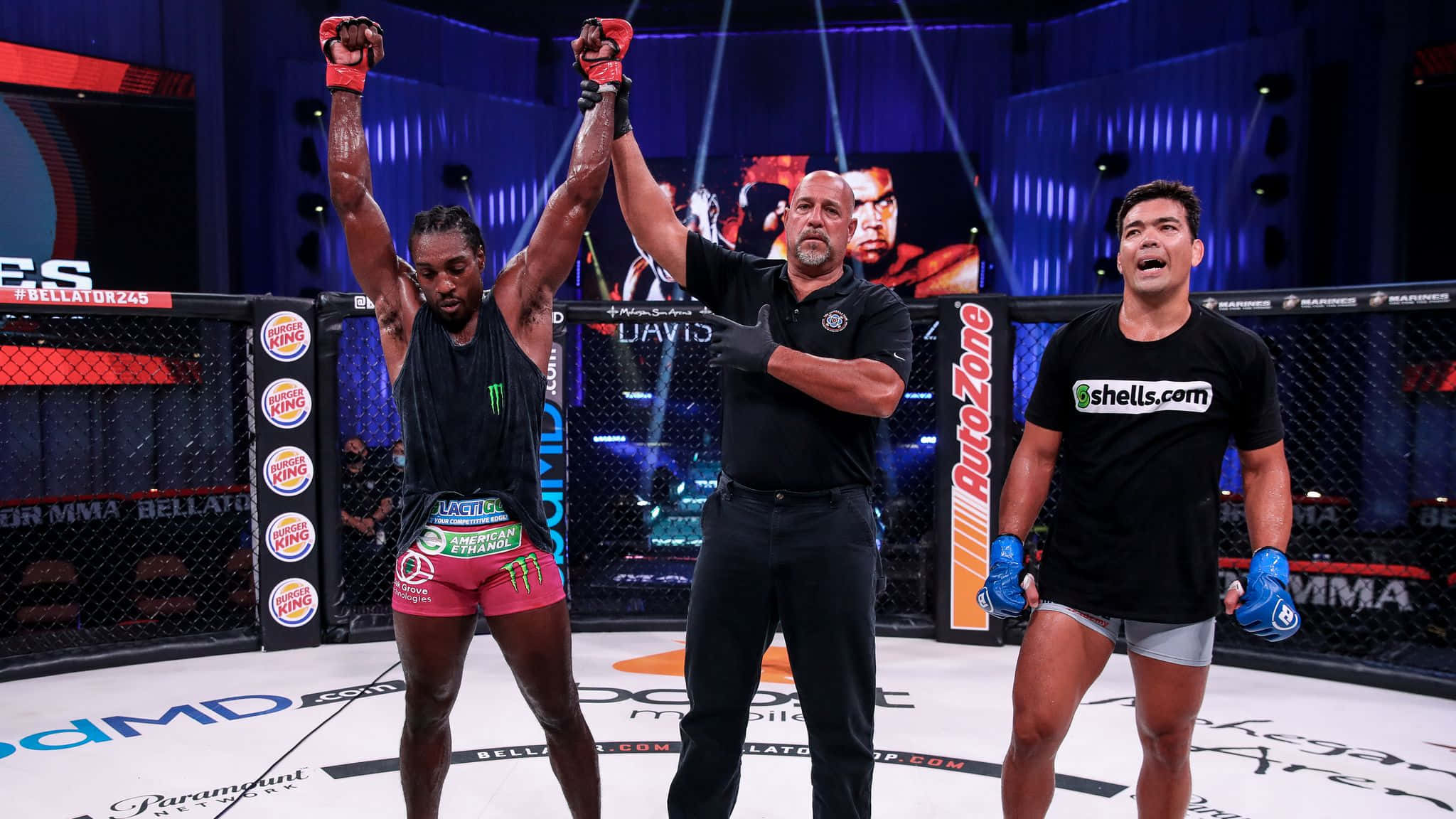 Lyoto Machida 參與 Bellator 245 賽事 壁紙 — 一位勝利的MMA拳手在燈光明亮的八角籠中，裁判宣佈他為勝者時高舉雙臂。