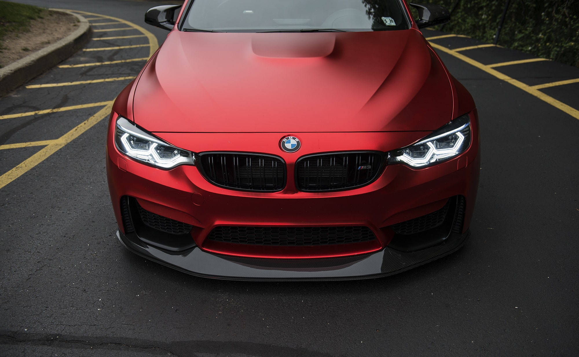 霧面紅色 M3 BMW 電腦壁紙 壁紙 — 一架啞光紅色BMW M4跑車停泊在鋪有黃線和綠化背景的停車場。