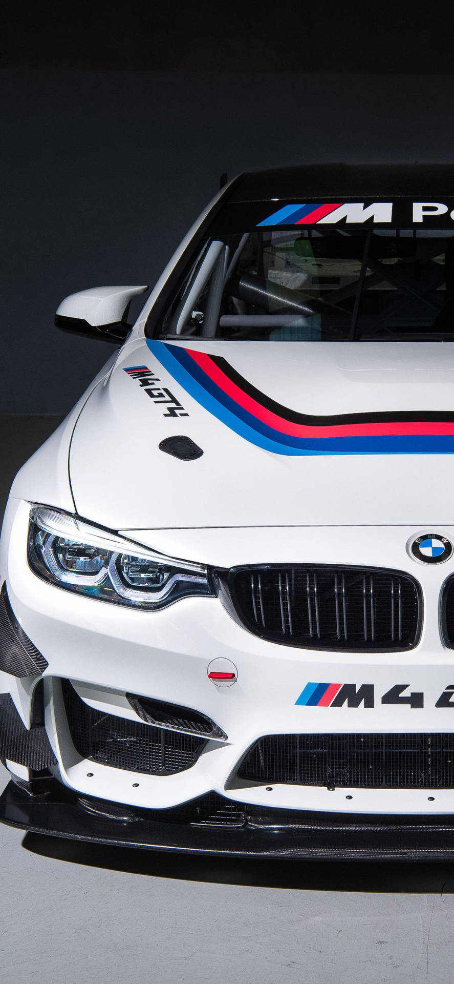 白色BMW M4賽車，帶有藍、紅、黑賽車條紋，在攝影棚燈光下。