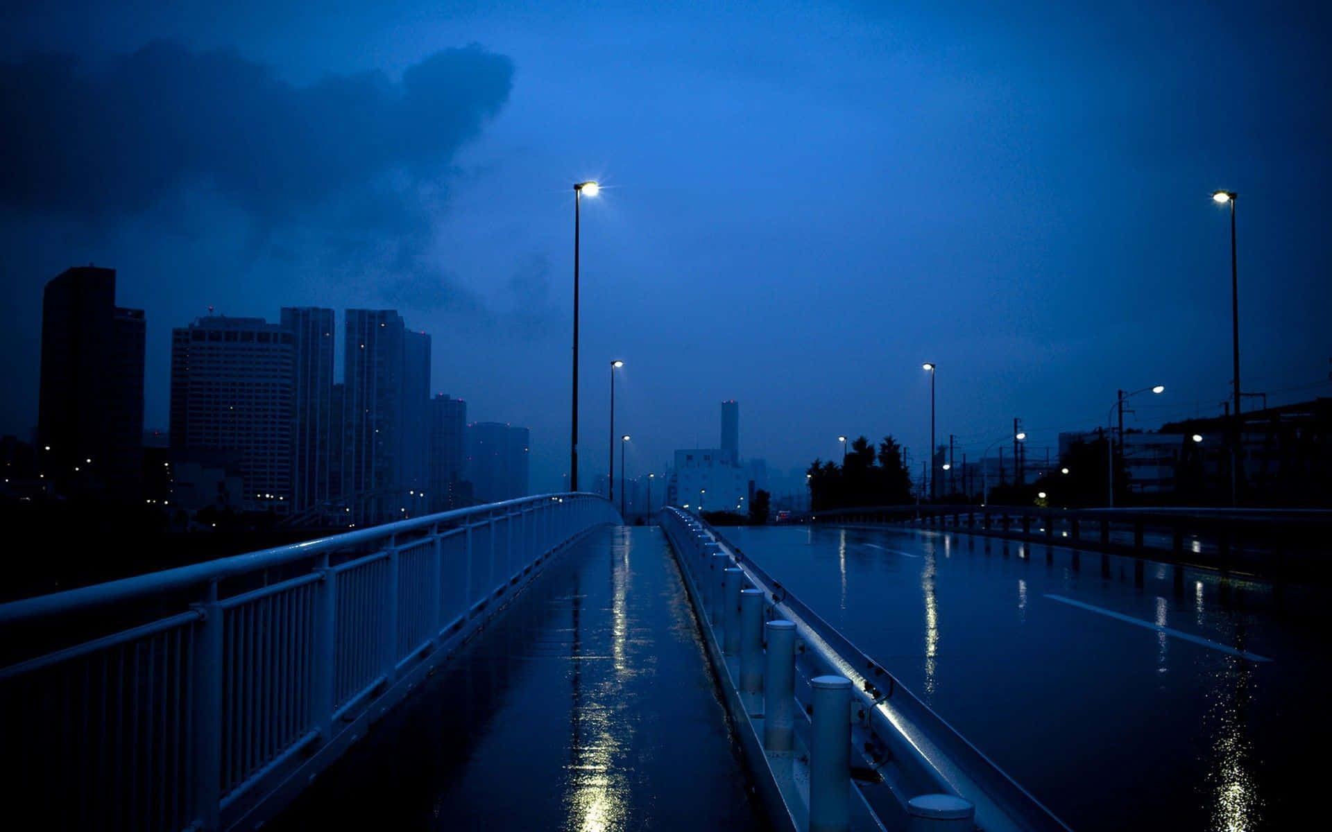 Mac 上的龐克風格 壁紙 — 在深藍色天空下，黃昏時分濕漉漉的城市橋樑，街燈倒映在雨水濕滑的路面上。