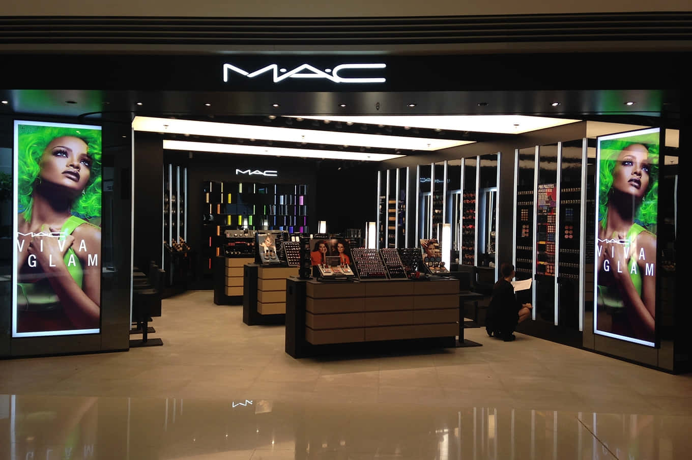 展現大膽美麗，Mac Cosmetics為您加持 壁紙 — 一間時尚的MAC化妝品店，發光的綠色Viva Glam廣告兩側是拋光地板和展示櫃檯。