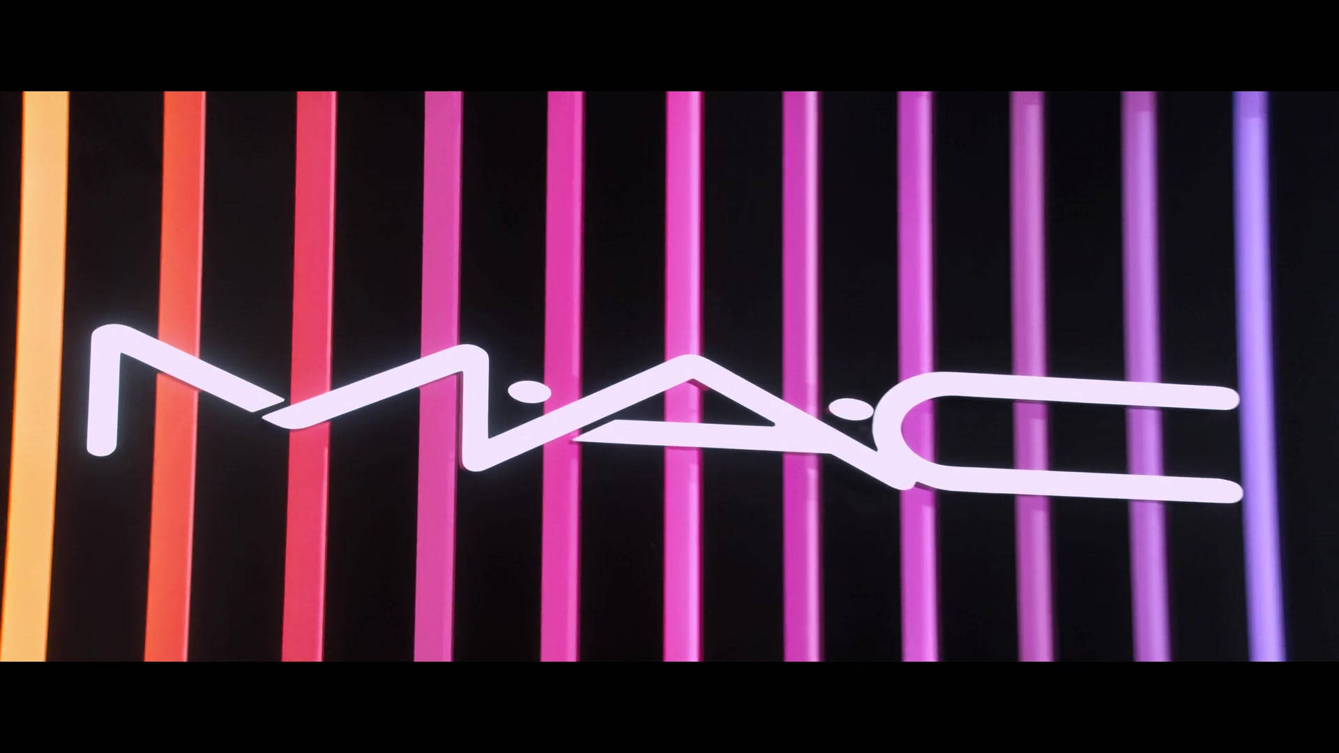 Mac Cosmetics 霓虹標誌 壁紙 — 一個發光的白色MAC標誌漂浮在垂直霓虹條紋的背景上，從橙色漸變到紫色。