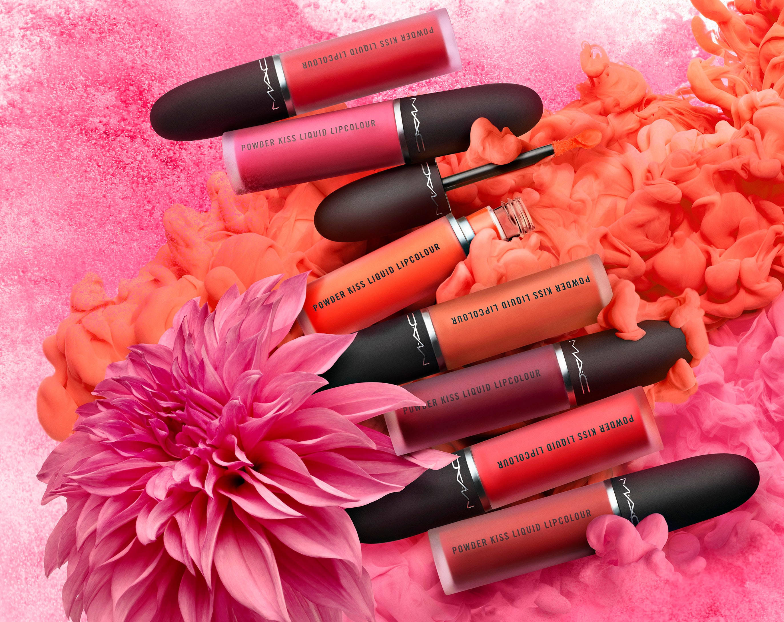 Mac Cosmetics 粉吻唇釉 壁紙 — 鮮豔的粉紅色和珊瑚色MAC唇膏藝術地排列在蓬鬆的花瓣和一朵大粉紅色大麗花上，背景是帶紋理的粉紅色。