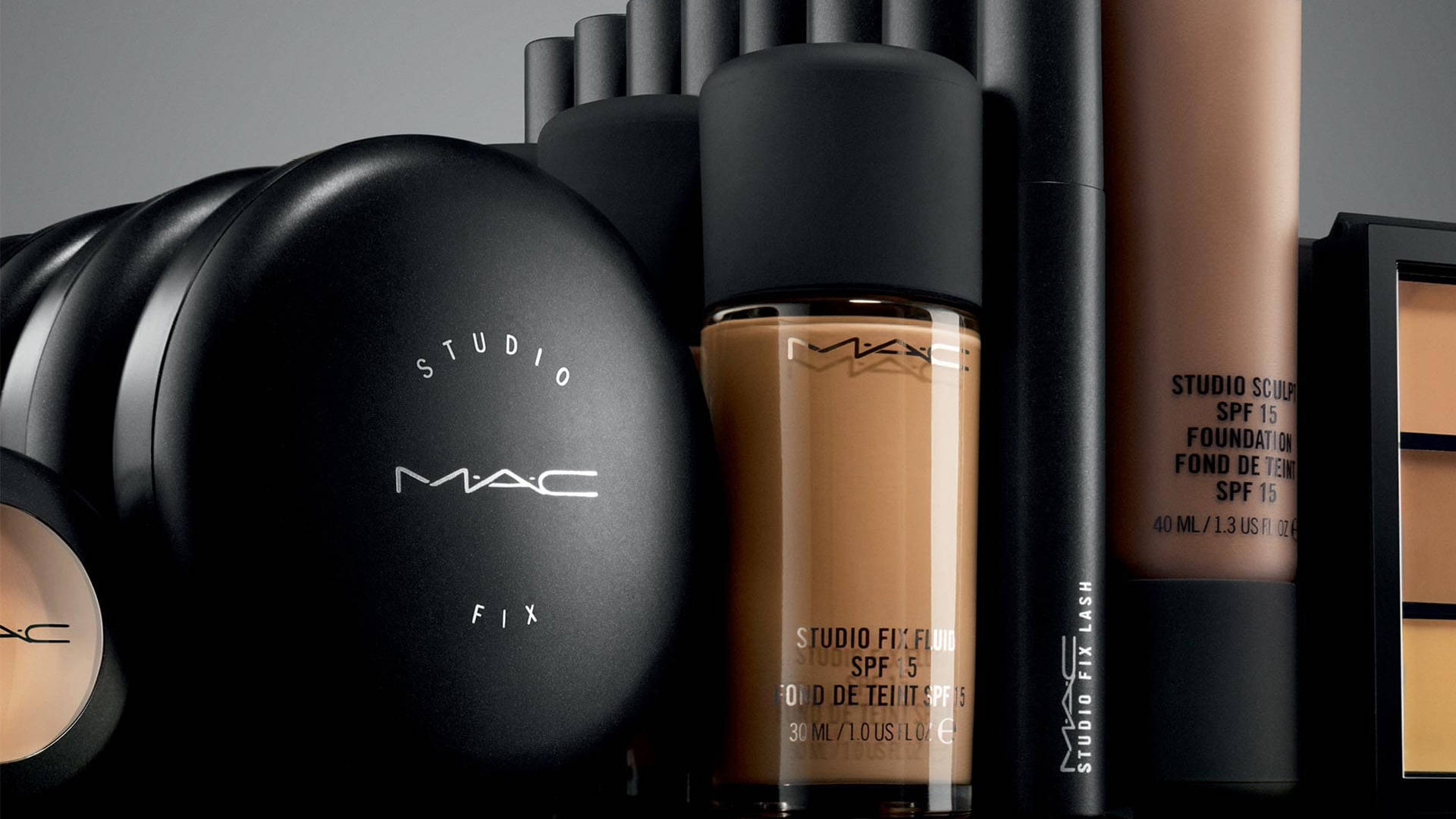 Mac Cosmetics 修飾底妝系列 壁紙 — 在簡約灰色背景上，黑色和米色調的MAC Studio Fix化妝產品的時尚排列。
