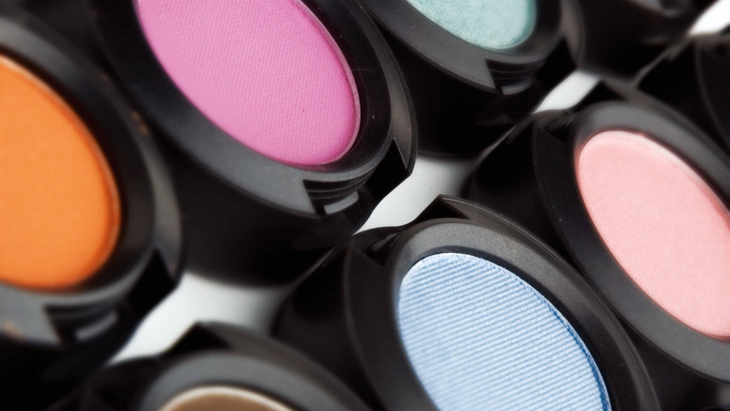 Mac Cosmetics 單色眼影 壁紙 — 粉紅、橙色、藍色和藍綠色鮮豔眼影盤的特寫，帶黑色蓋子，放在白色表面上。
