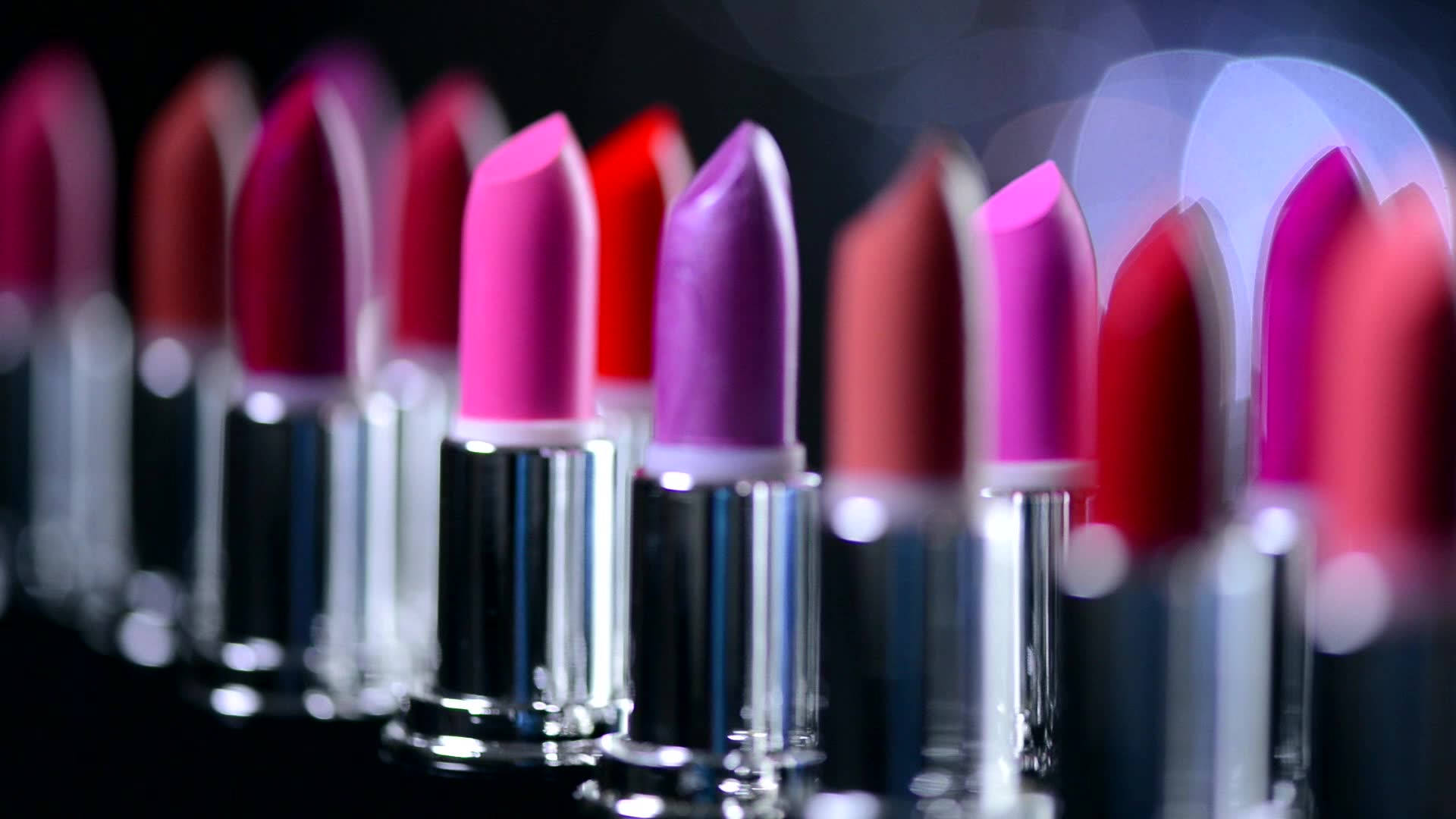 Mac Cosmetics 展櫃唇膏 壁紙 — 淺景深突出了在帶有散景燈光的深色背景上的鮮豔粉紅色和紫色唇膏。