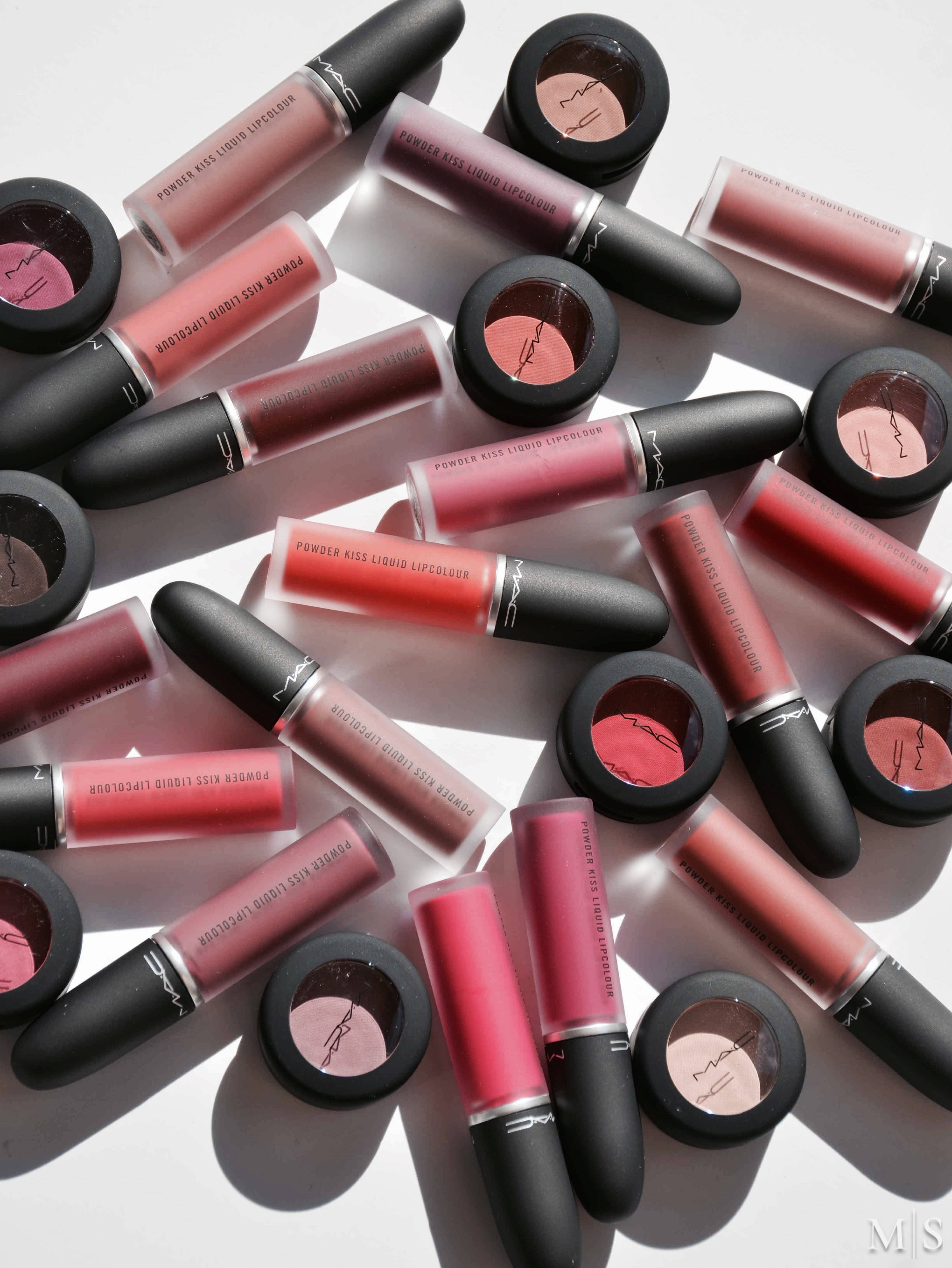 Mac Cosmetics 粉吻系列 壁紙 — 在明亮的白色表面上散落著一系列粉紅色和紅色調的MAC唇彩和眼影。