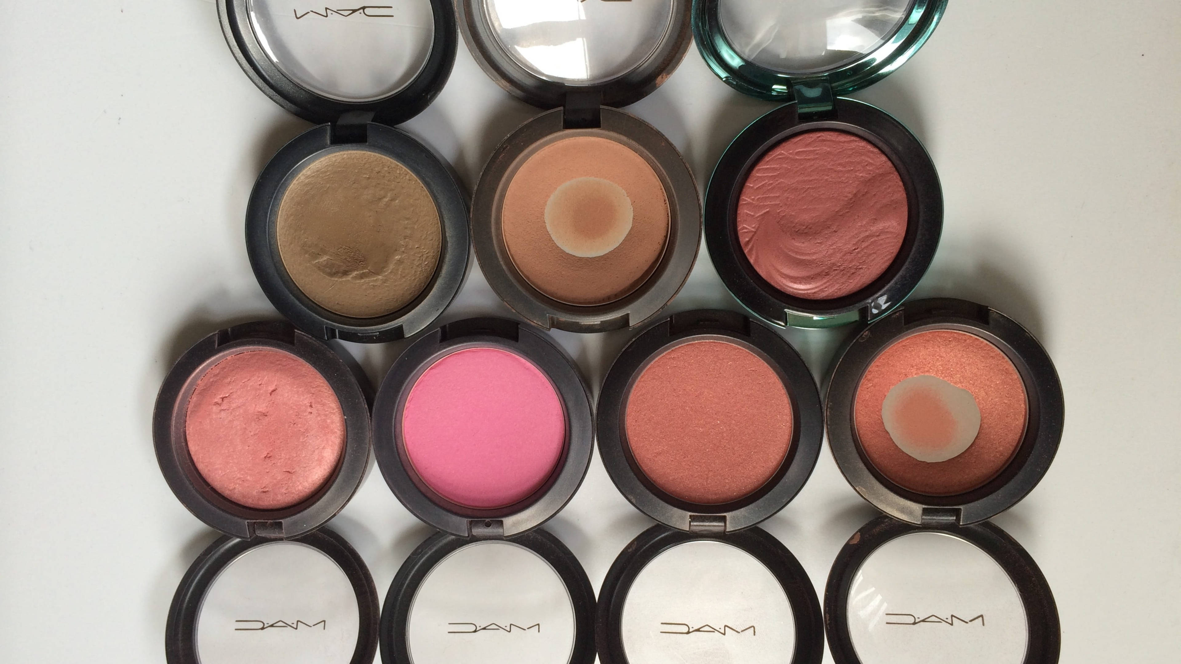 Mac Cosmetics 腮紅與修容系列 壁紙 — 從上方俯瞰十個打開的MAC胭脂粉盒，整齊排列在白色表面上，展示從啞光到閃爍的各種色調。
