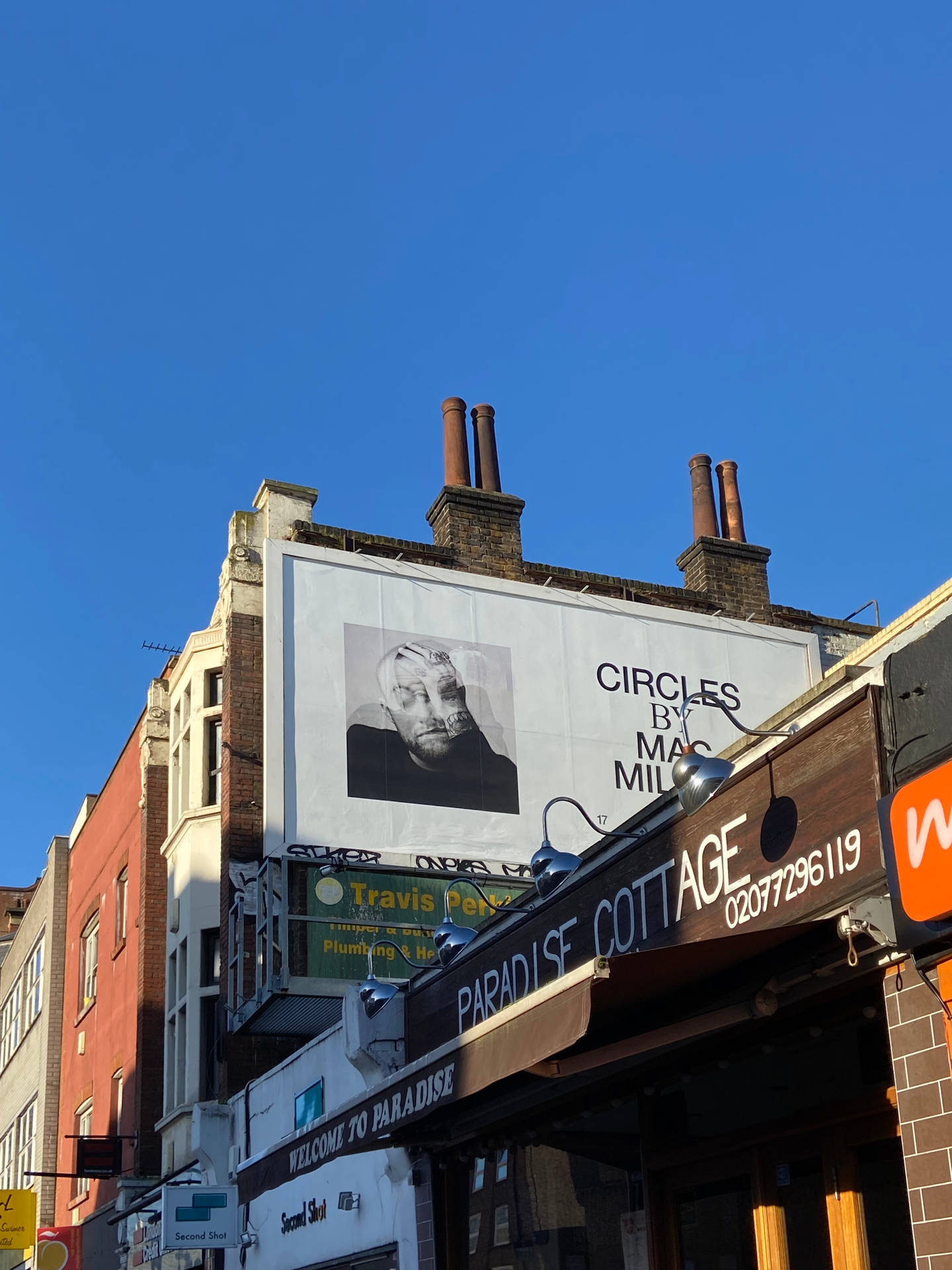 城市街景，有一個大型廣告牌，顯示一個男人的肖像和mac miller的文字圓圈。