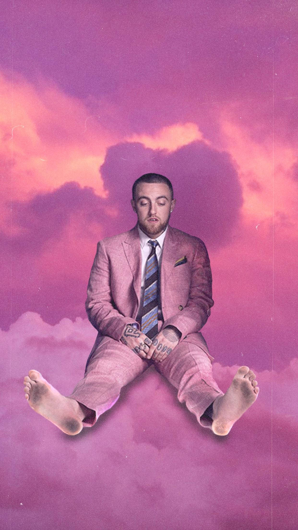 Mac Miller 穿粉紅西裝踩雲朵 壁紙 — 一名身穿粉紅色西裝的男子赤腳坐在雲上，背景是夢幻的粉紅色和橙色天空。