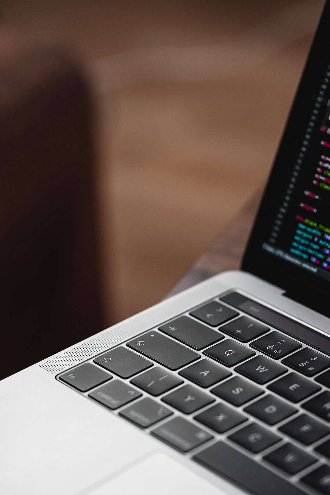 MacBook Air 2020 近距離特寫 壁紙 — 銀色手提電腦鍵盤的特寫，屏幕上顯示彩色代碼滾動，背景為模糊的木質。
