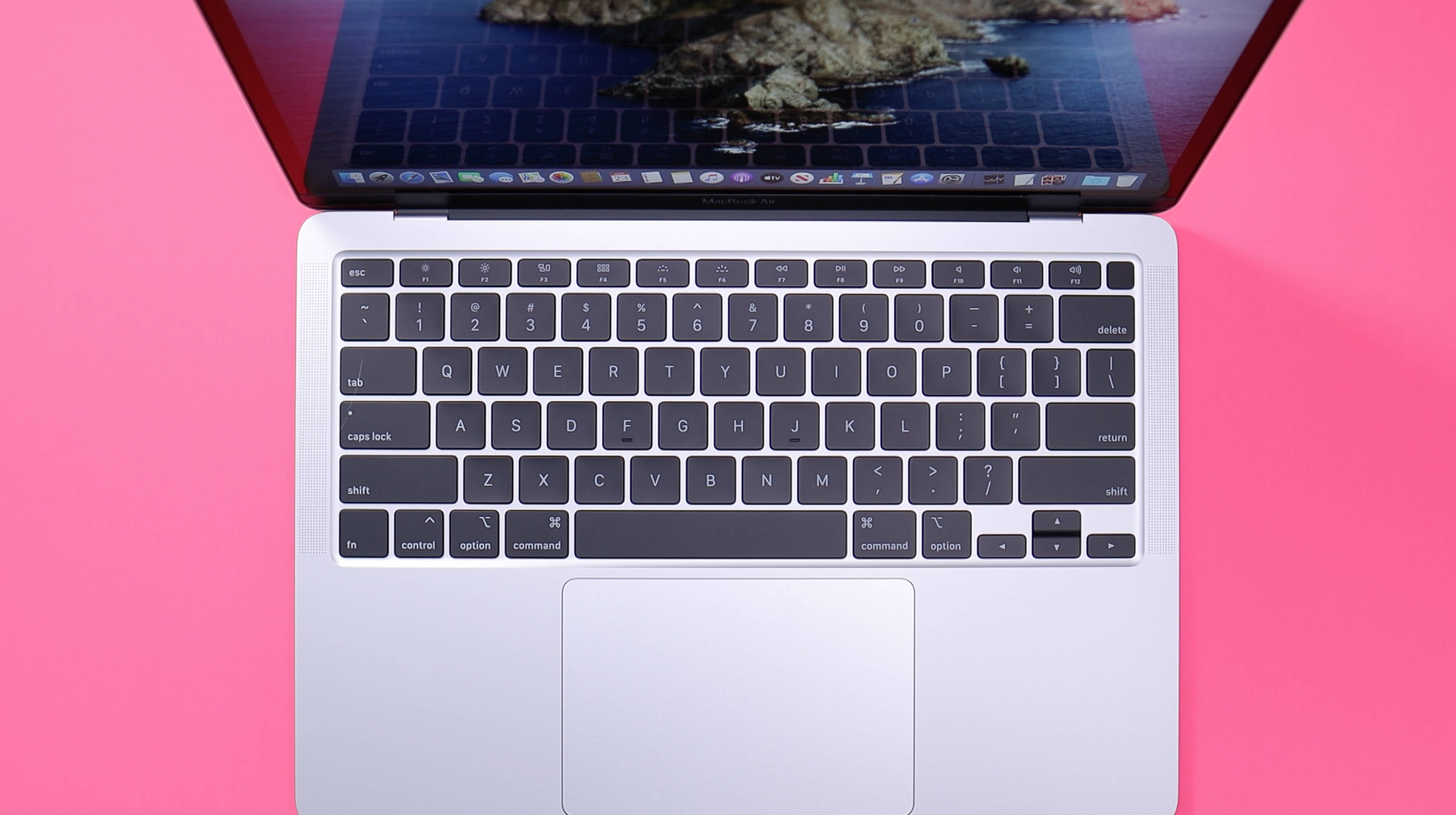 MacBook Air 2020粉紅色表面 壁紙 — 銀色手提電腦配黑色鍵盤打開，放在鮮豔粉紅色背景上，顯示海洋壁紙。