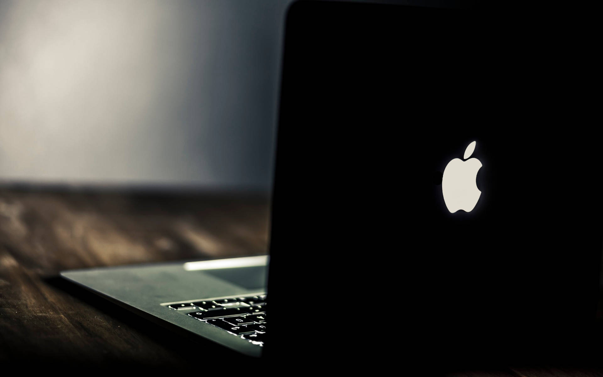 昏暗光線下木桌上帶發光Apple標誌的黑色手提電腦