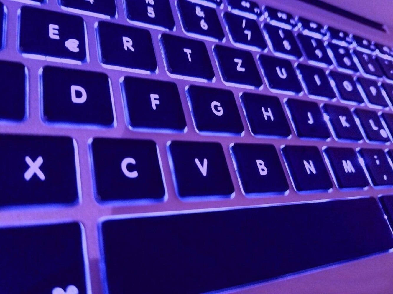MacBook背光鍵盤美學 壁紙 — 手提電腦鍵盤嘅特寫，沐浴喺冷紫色背光入面，突顯按鍵同銀色邊框。