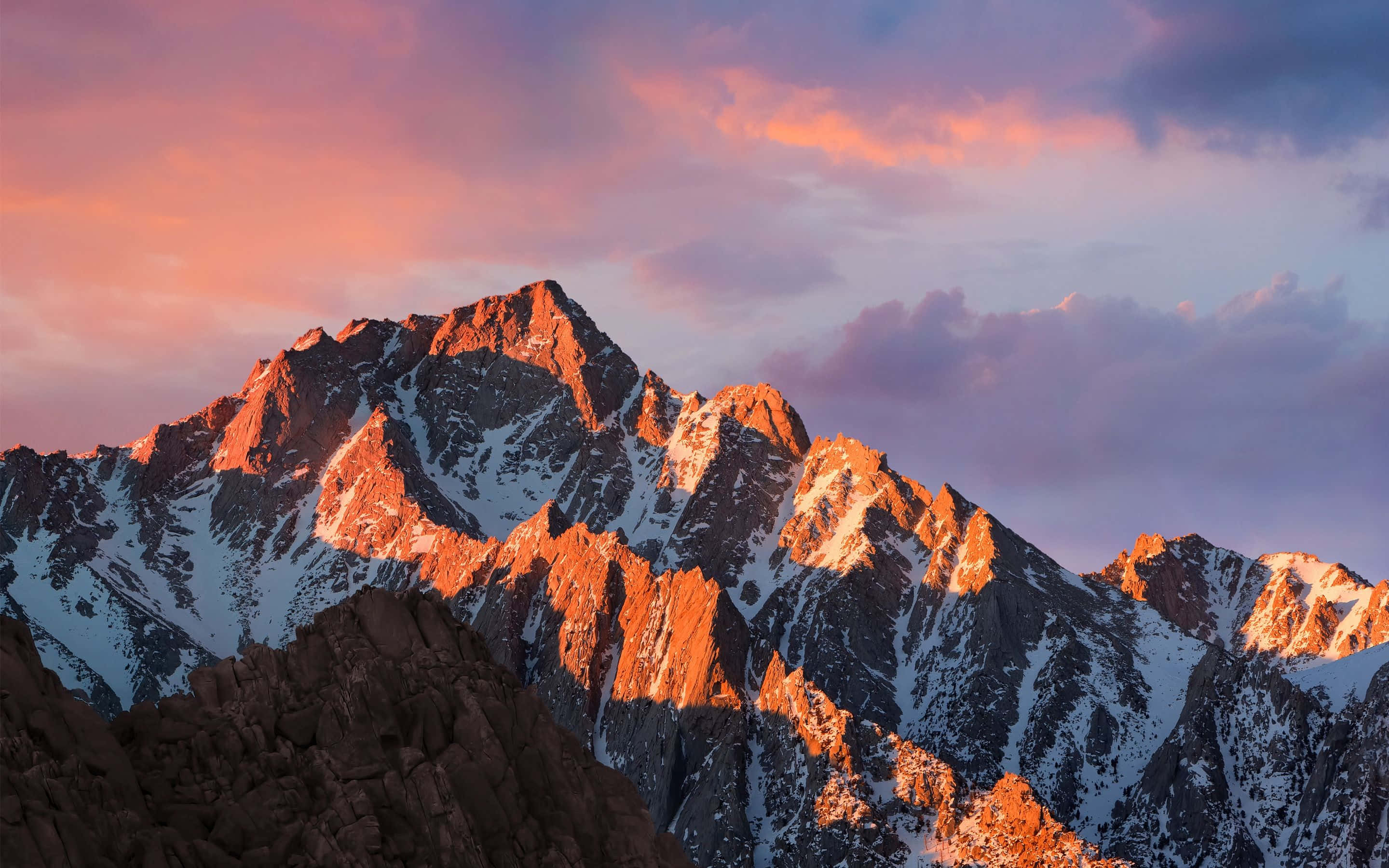 孤松峰 MacBook預設背景 壁紙 — 白雪覆蓋的山峰在溫暖的夕陽光下閃耀，映襯著充滿活力的粉紅色和紫色天空。