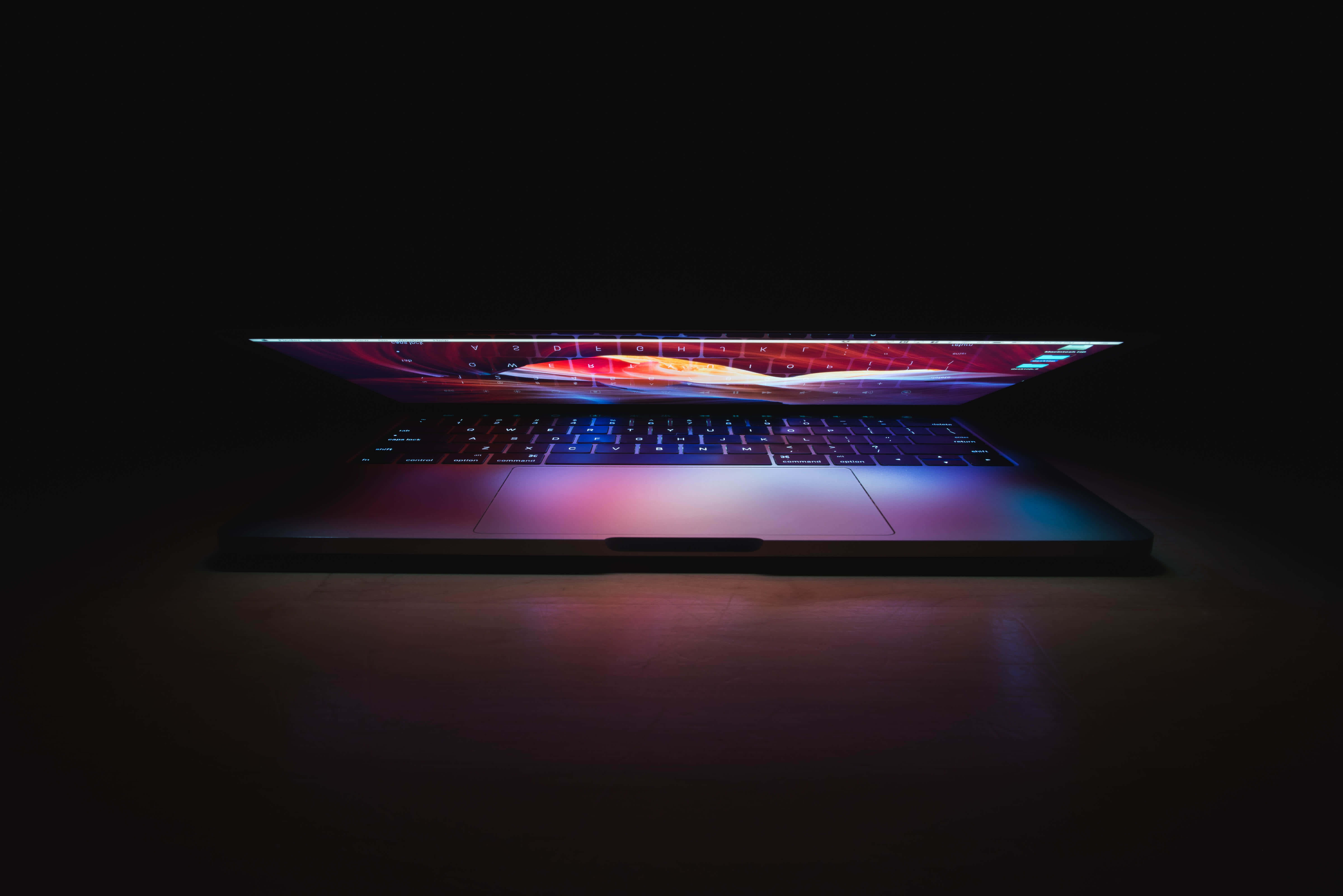 用美學 MacBook 提升你嘅風格 壁紙 — 一部時尚的筆記型電腦在黑暗背景上，螢幕和鍵盤散發出充滿活力的抽象光芒。