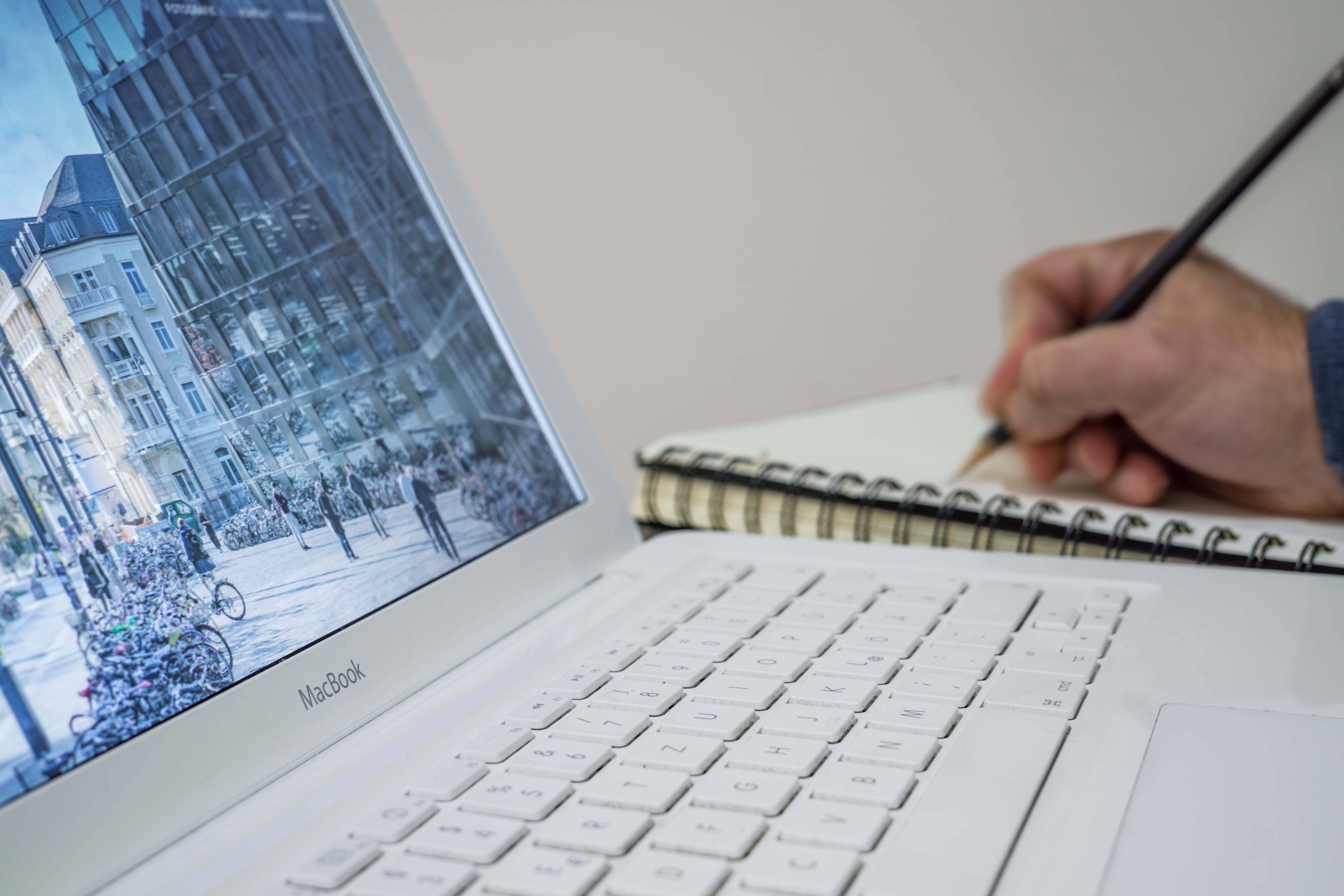 時尚現代的MacBook，兼具美學與科技 壁紙 — 一隻手在筆記本上素描，旁邊的筆記型電腦顯示一個繁忙的歐洲街景，有自行車和歷史建築。