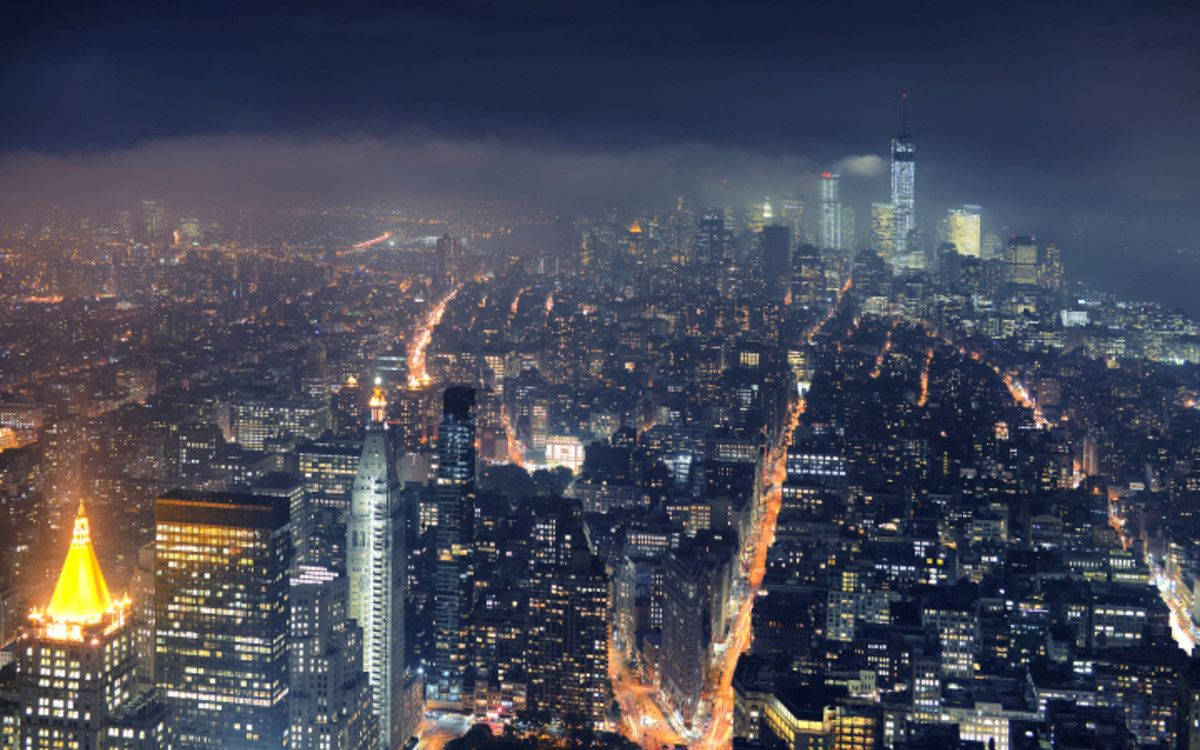 MacBook Pro 高譚市夜景 壁紙 — 夜晚鳥瞰廣闊的城市景觀，摩天大樓閃爍，街道燈火通明，天空陰暗多雲。
