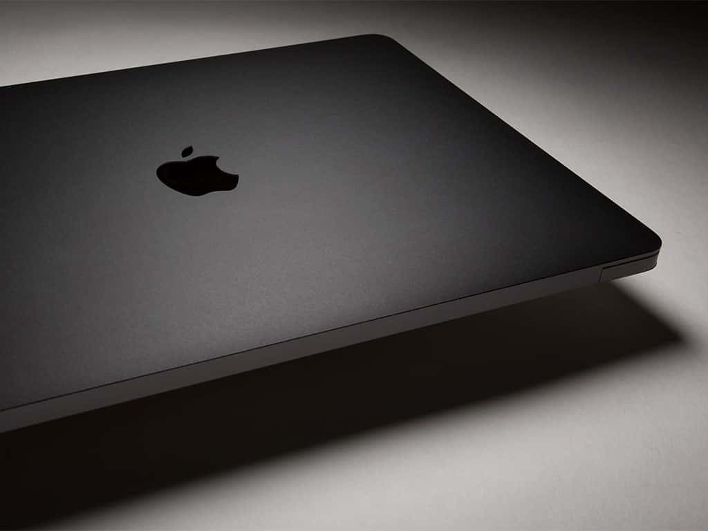 銀色標誌對比黑色背景的MacBook Pro，隨時待命 壁紙 — 一部時尚的啞光黑色筆記型電腦，帶有簡約的Apple標誌，在柔和的工作室燈光下傾斜放置。