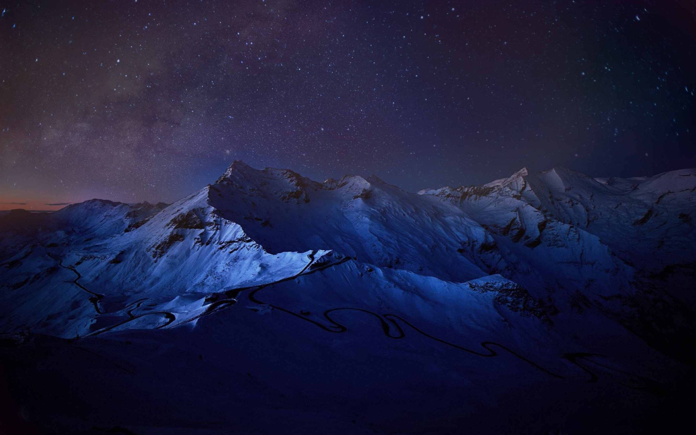 MacBook Pro 夜空冰山 壁紙 — 白雪覆蓋的山脈在繁星點點的夜空下，蜿蜒的道路在銀河下閃耀。