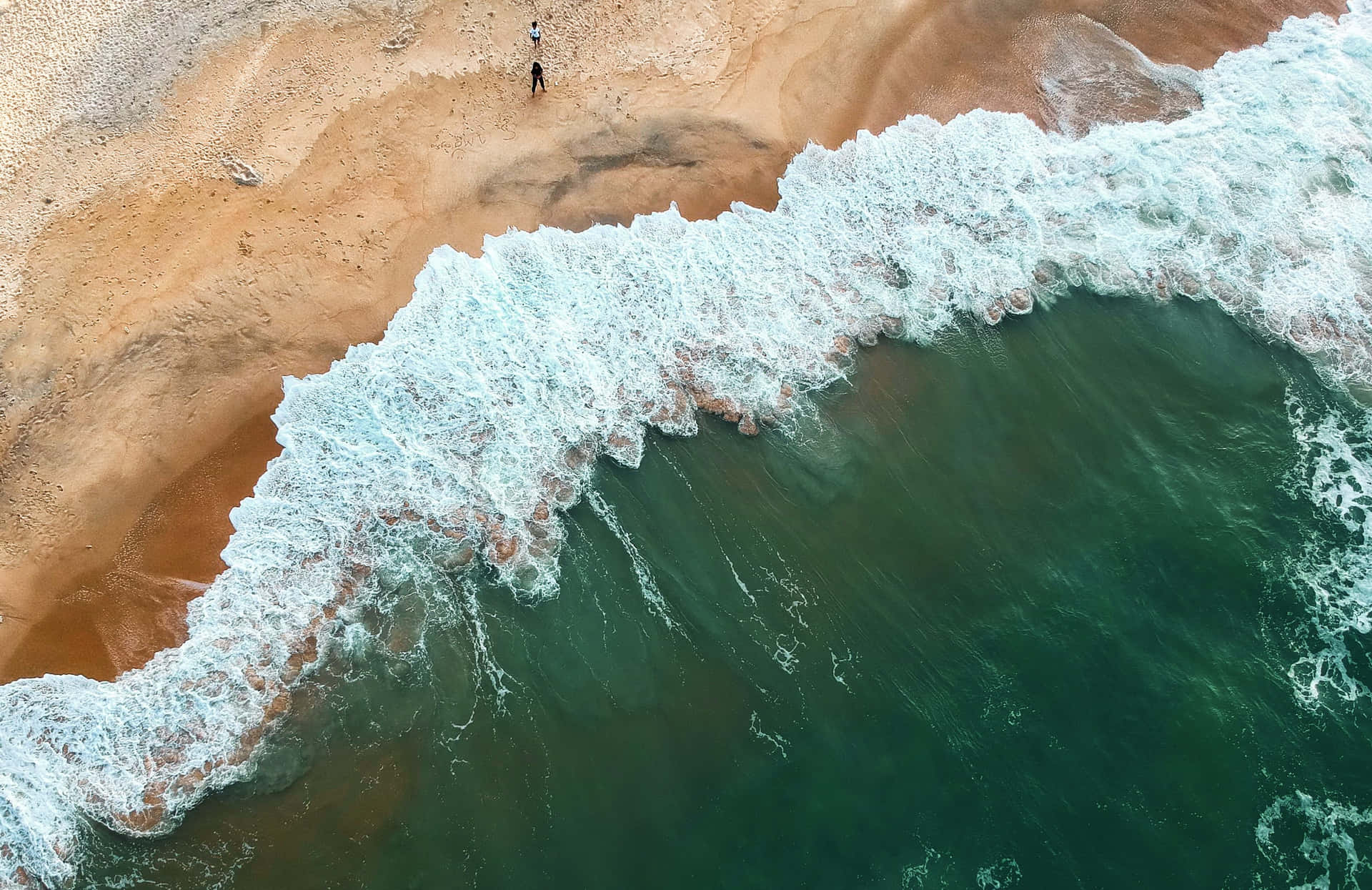 兩個人在沙灘上行走，海浪拍打著海岸。