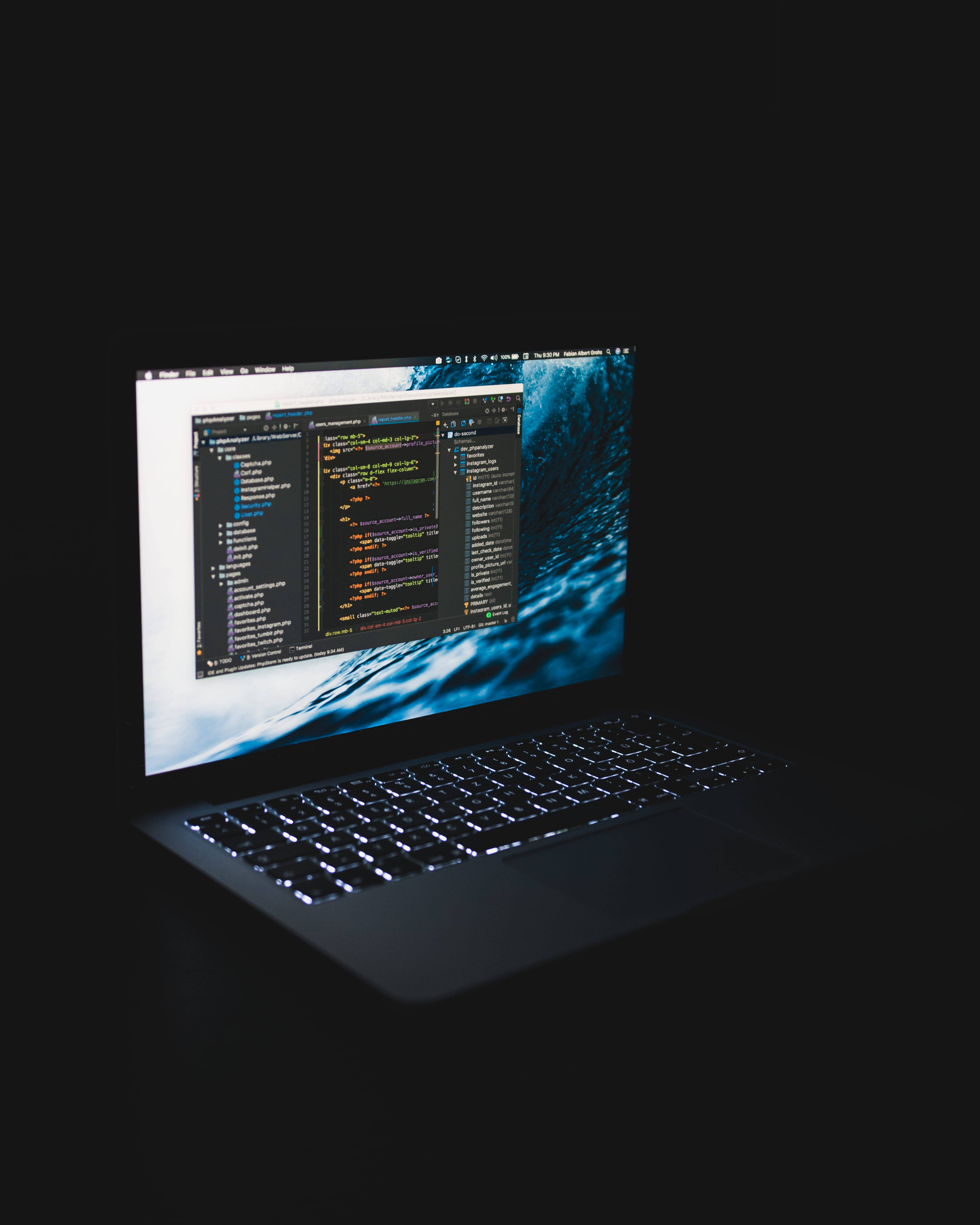 MacBook 上的程式設計 壁紙 — 黑暗中的手提電腦在藍色海浪壁紙上顯示發光的代碼。