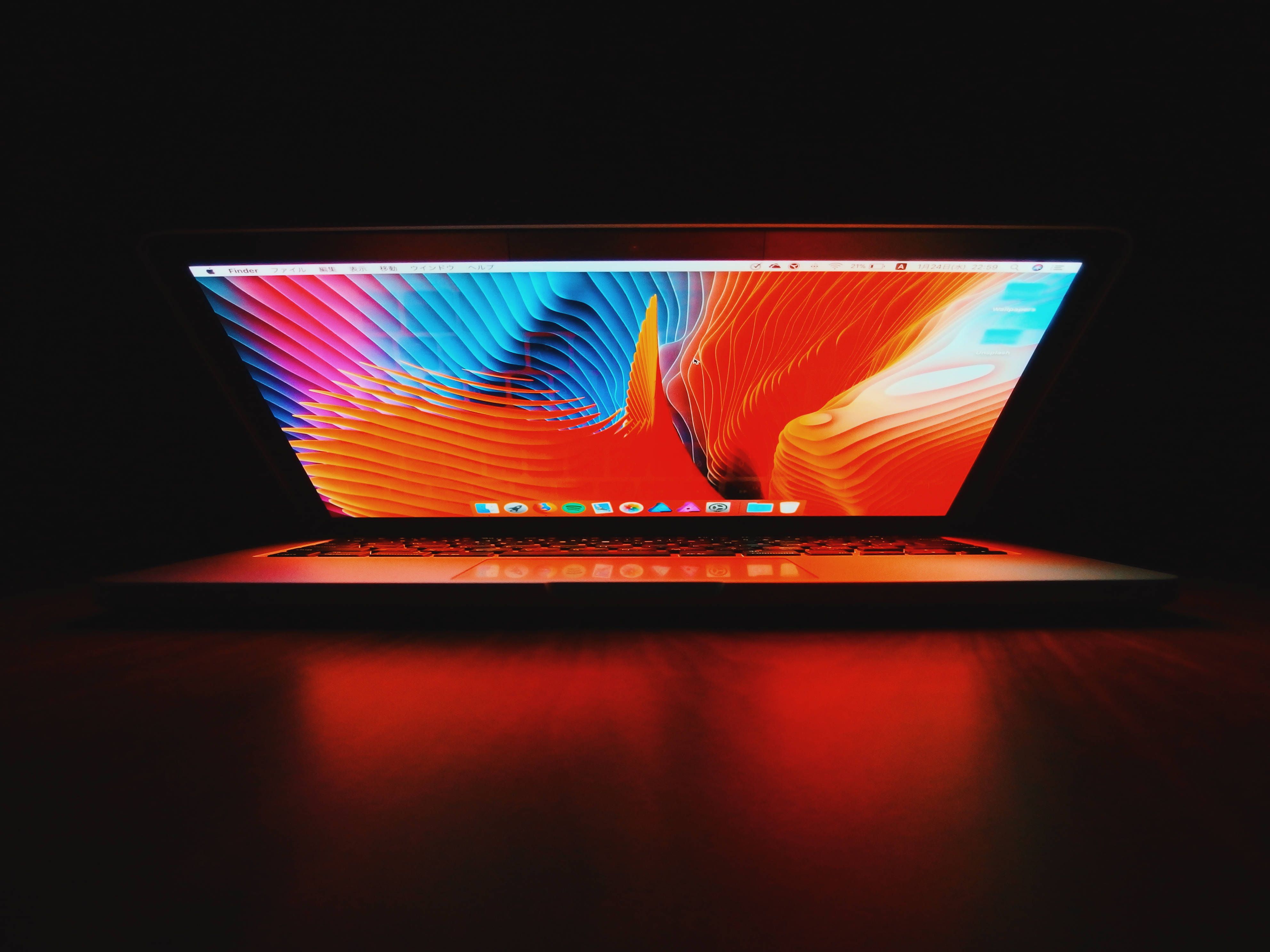MacBook紅屏 壁紙 — 一部時尚的筆記型電腦在深色背景下散發出充滿活力的抽象色彩波浪。