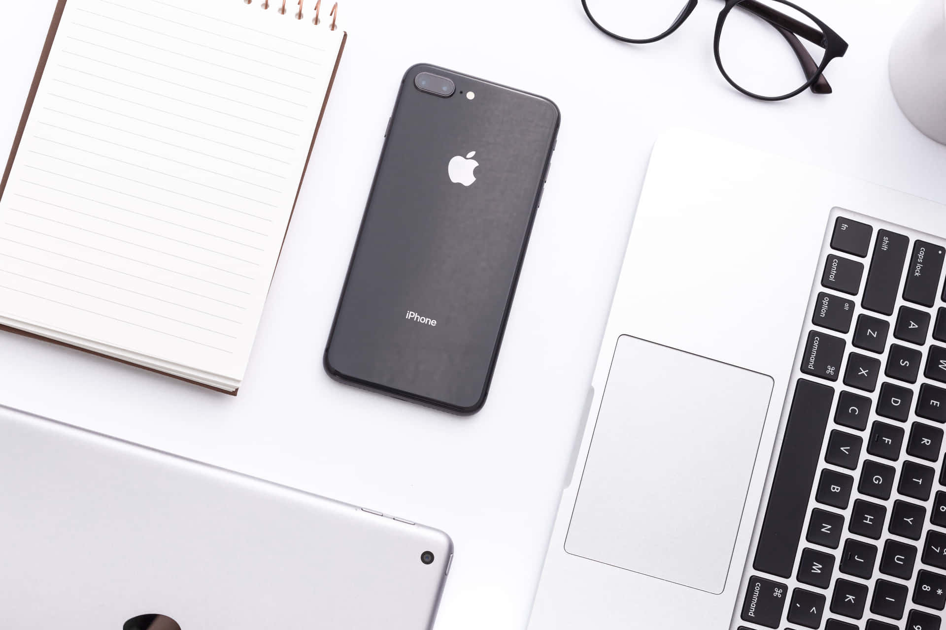 整潔現代的桌面，配有手提電腦、iPhone、筆記本和眼鏡