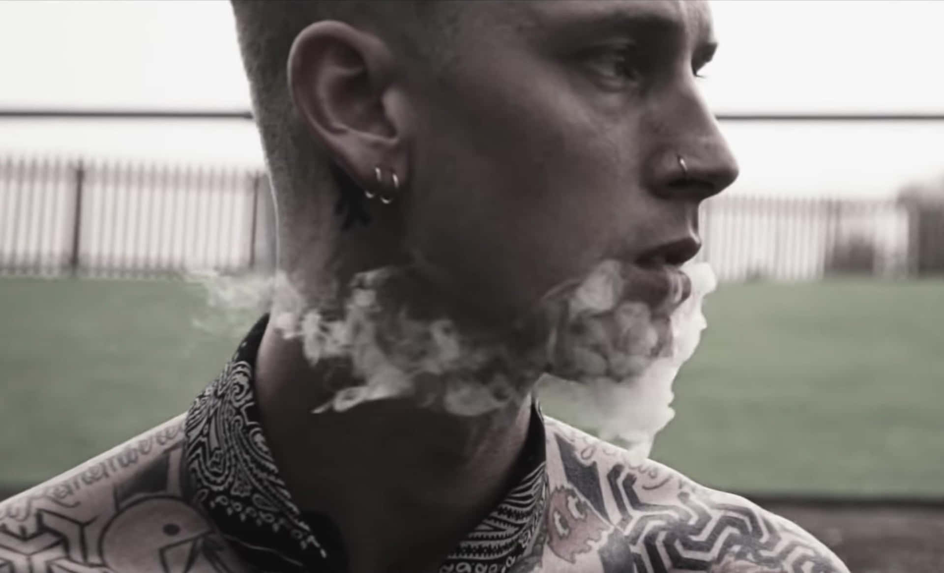 紋身男子在戶外呼出煙霧，戴著頭巾和耳環