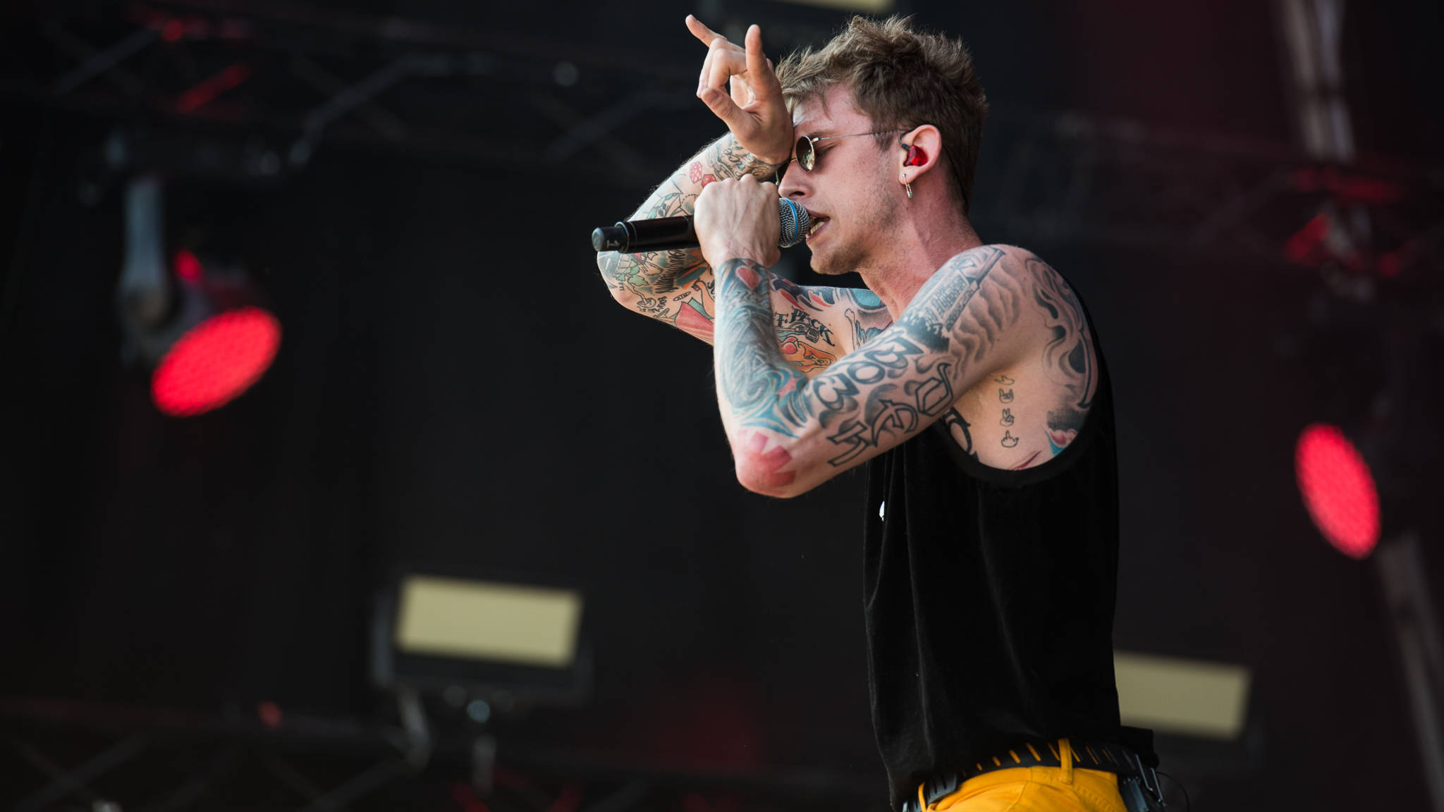 Machine Gun Kelly演唱會 壁紙 — 一位有紋身的男歌手在紅色舞台燈光下熱情地拿著麥克風表演。