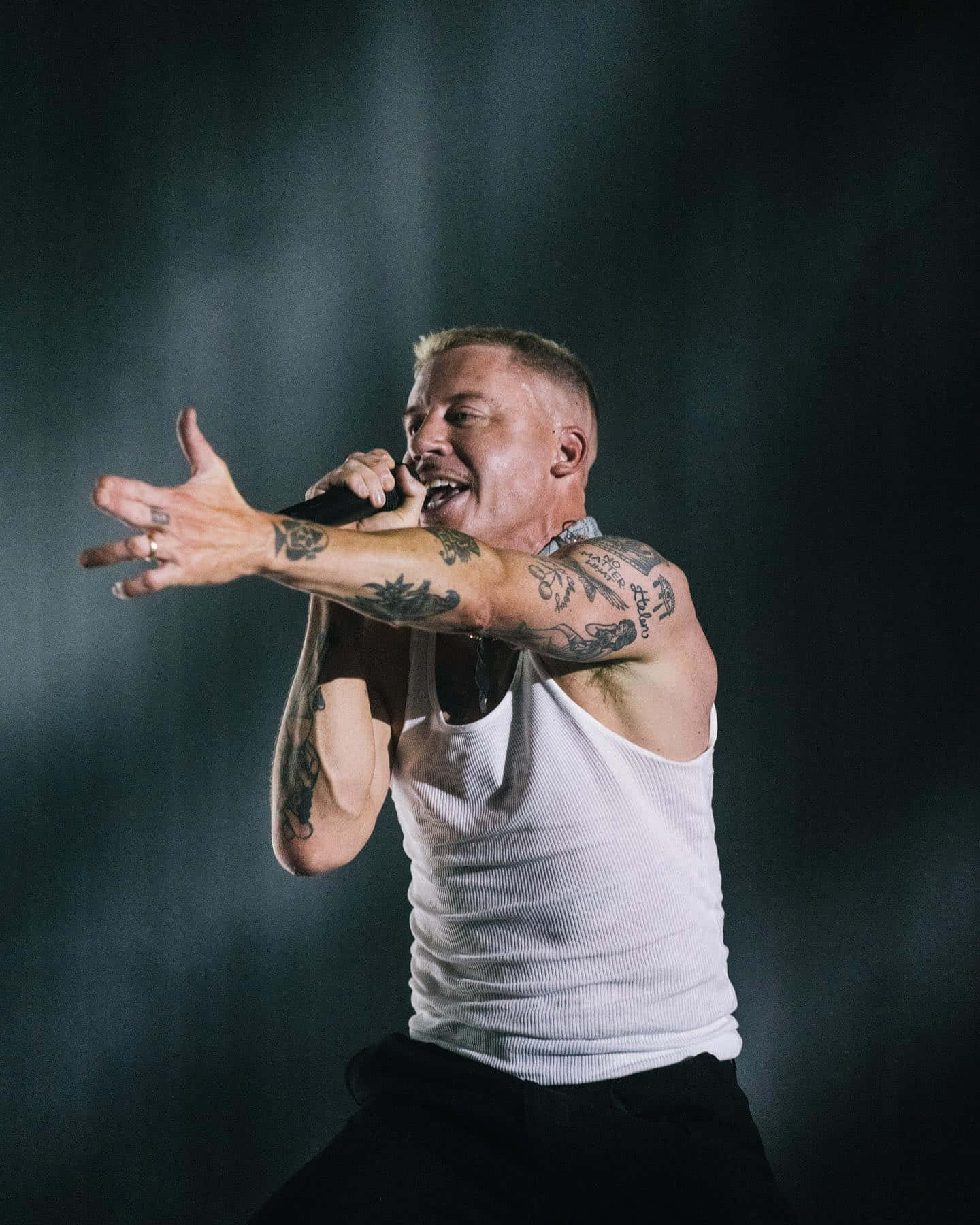 Macklemore 舞台現場演出 壁紙 — 一位紋身男歌手身穿白色背心，在舞台燈光下對著麥克風熱情演唱，身後煙霧繚繞。